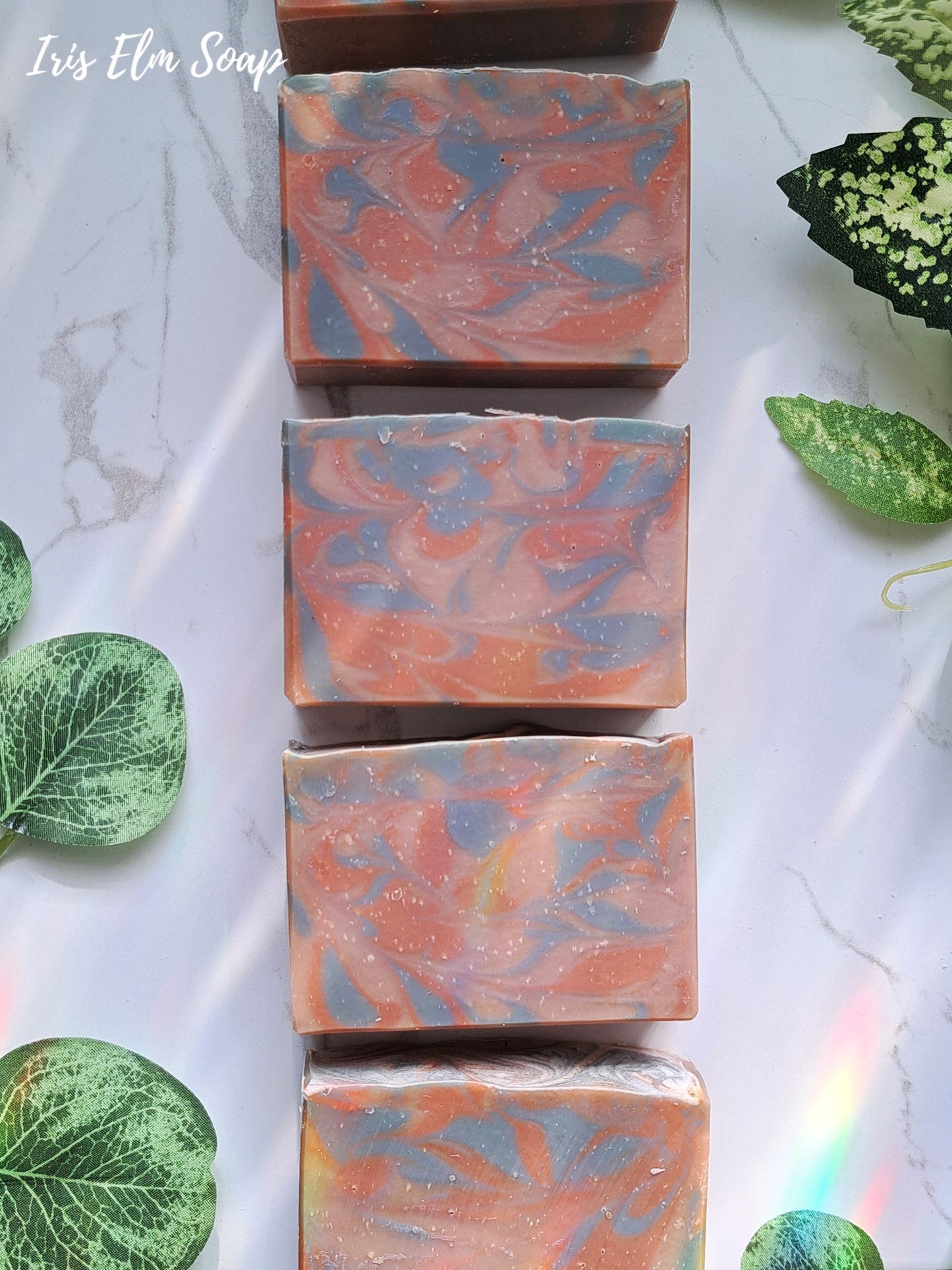 Marbled amber rosewood handmade soap bars on a marble surface with green leaves