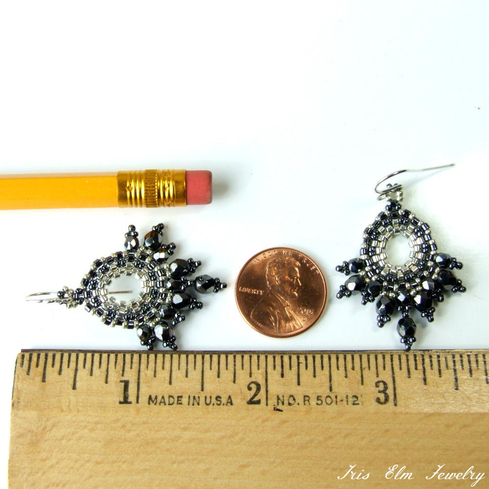Pair of dark grey beaded glass earrings next to a penny and a ruler for size comparison on a white background.