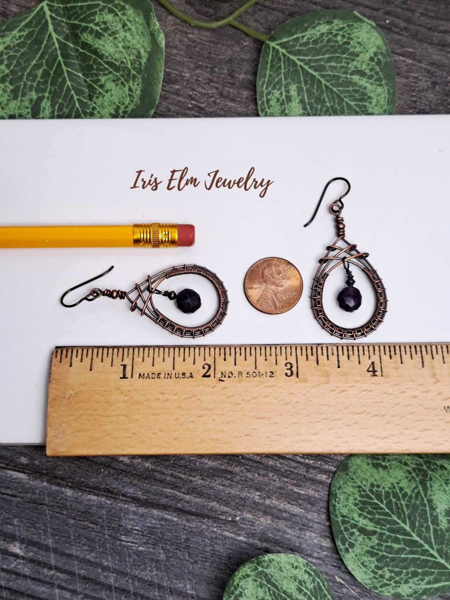 Pair of 2.25 inch long earrings on a ruler with 'Iris Elm Jewelry' branding, surrounded by green leaves.