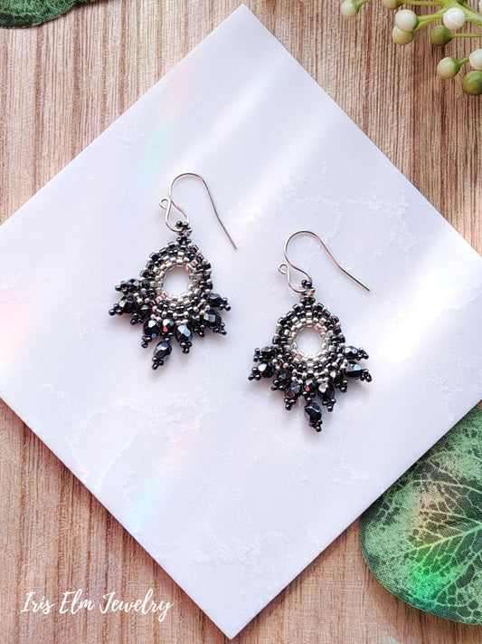 Pair of beaded dark grey czech glass fan earrings on a white napkin with 'Iris Elm Jewelry' branding.