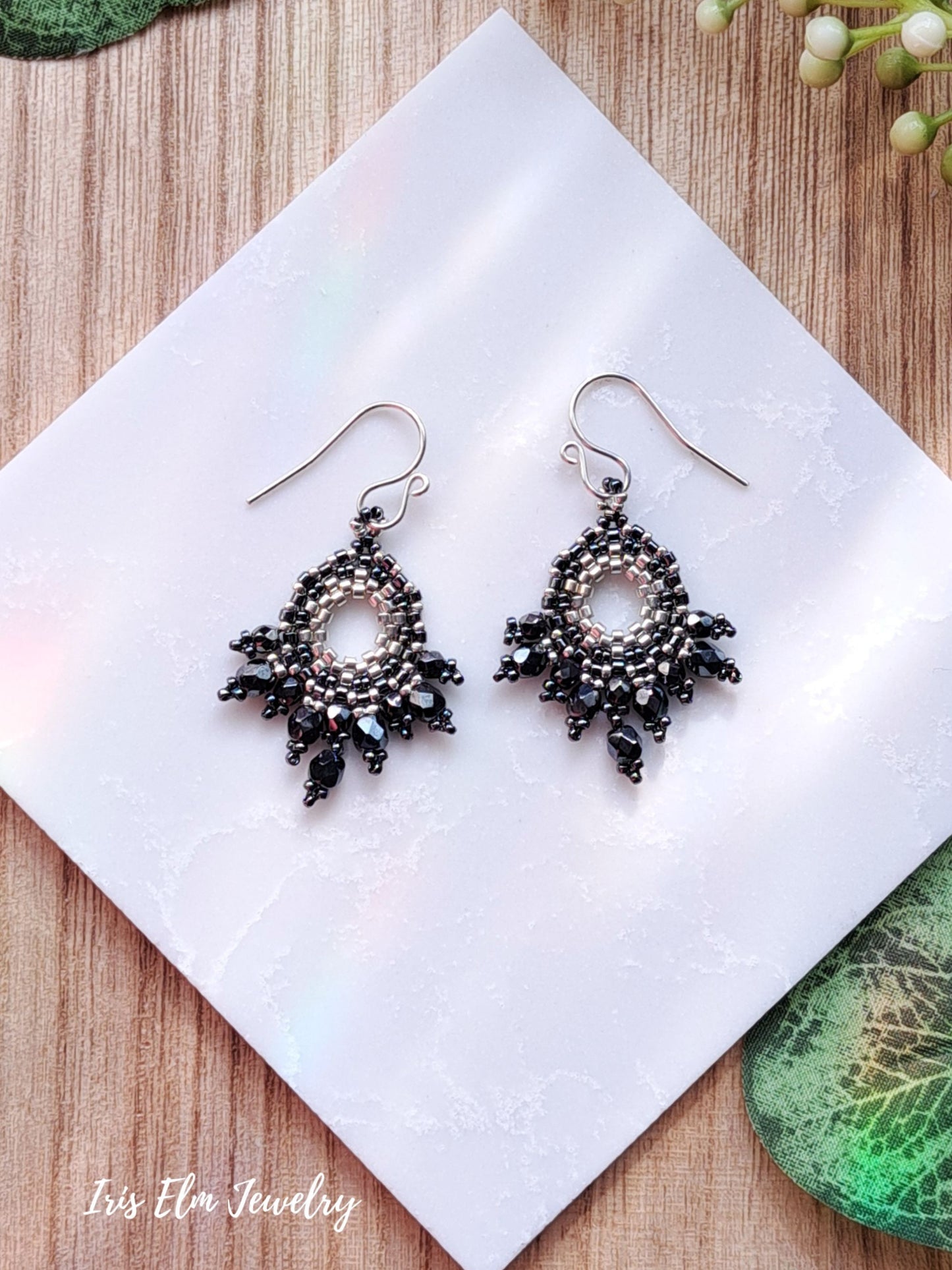 Pair of dark grey glass beadwork beaded earrings on a white napkin with 'Iris Elm Jewelry' branding.