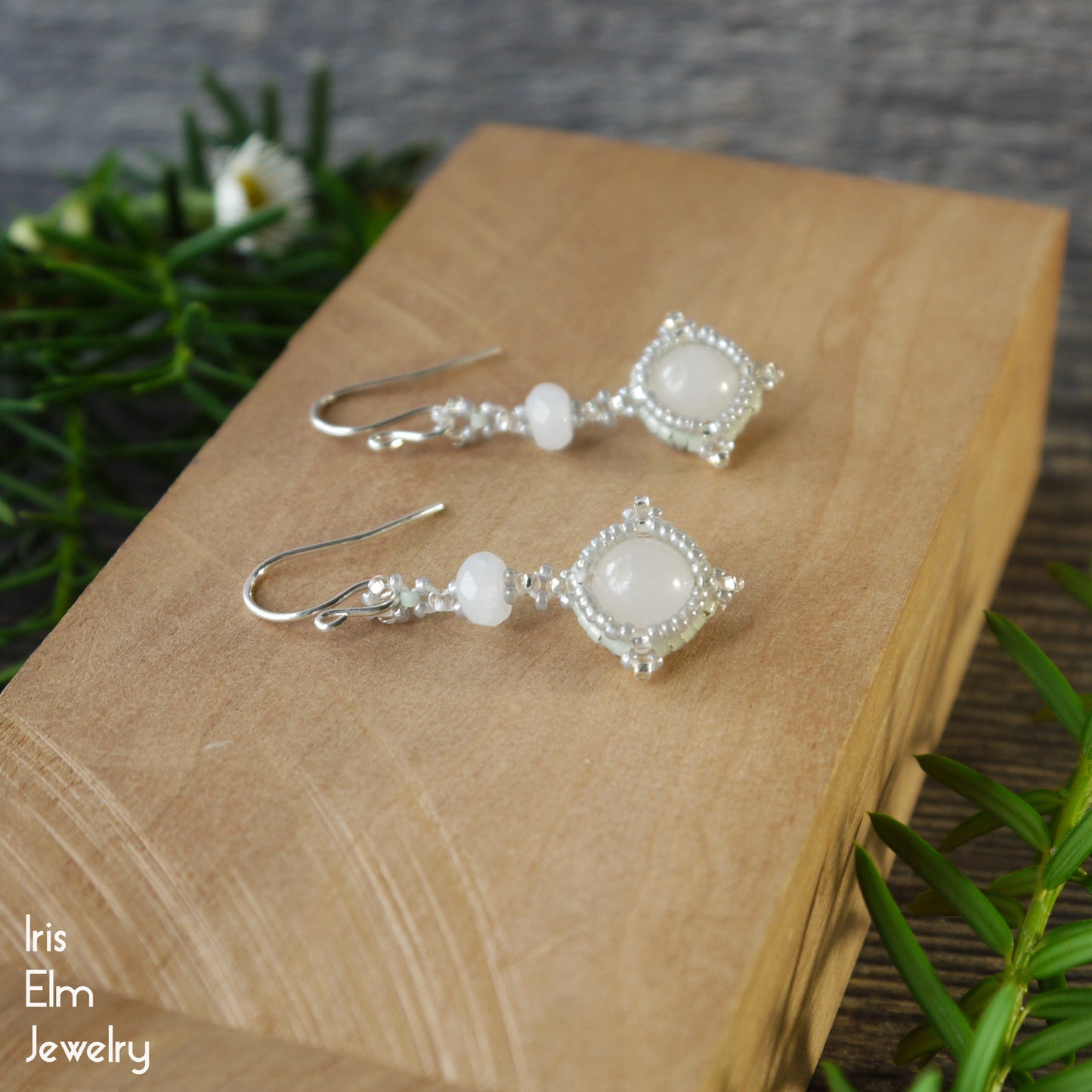 Beaded white quartz drop gemstones earrings on a wooden block, featuring 'Iris Elm Jewelry' branding.