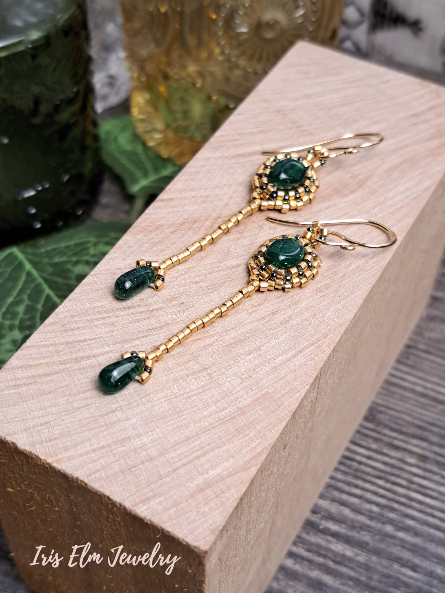 Gold earrings with green aventurine gemstones on a wooden block, branded 'Iris Ela Jewelry'.