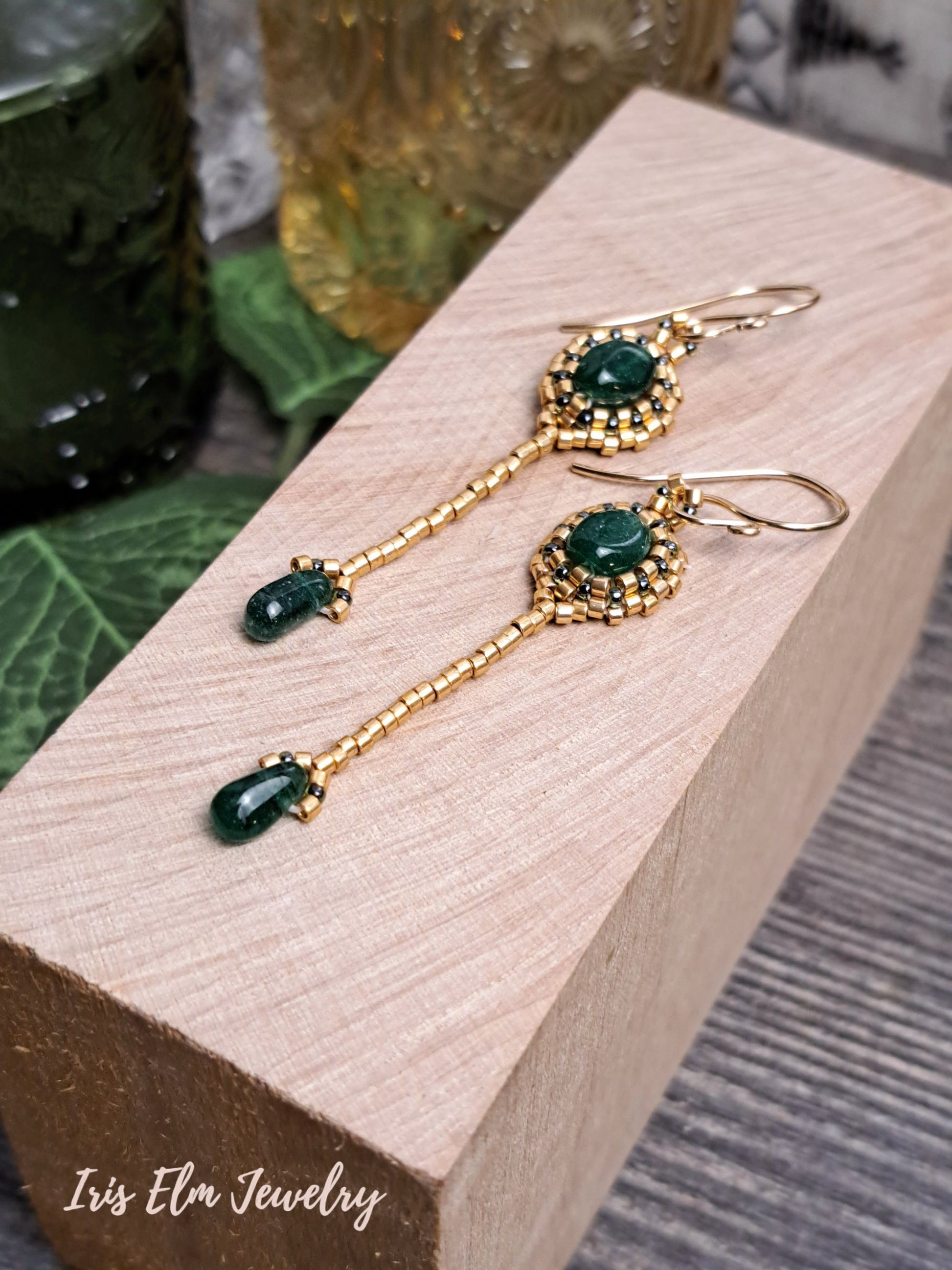 Gold earrings with green aventurine gemstones on a wooden block, branded 'Iris Ela Jewelry'.