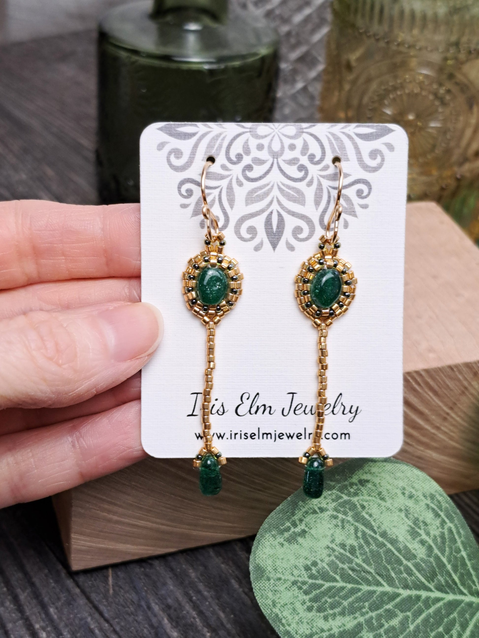 Gold and green aventurine earrings on a 'Iris Elm Jewelry' card held by a hand.