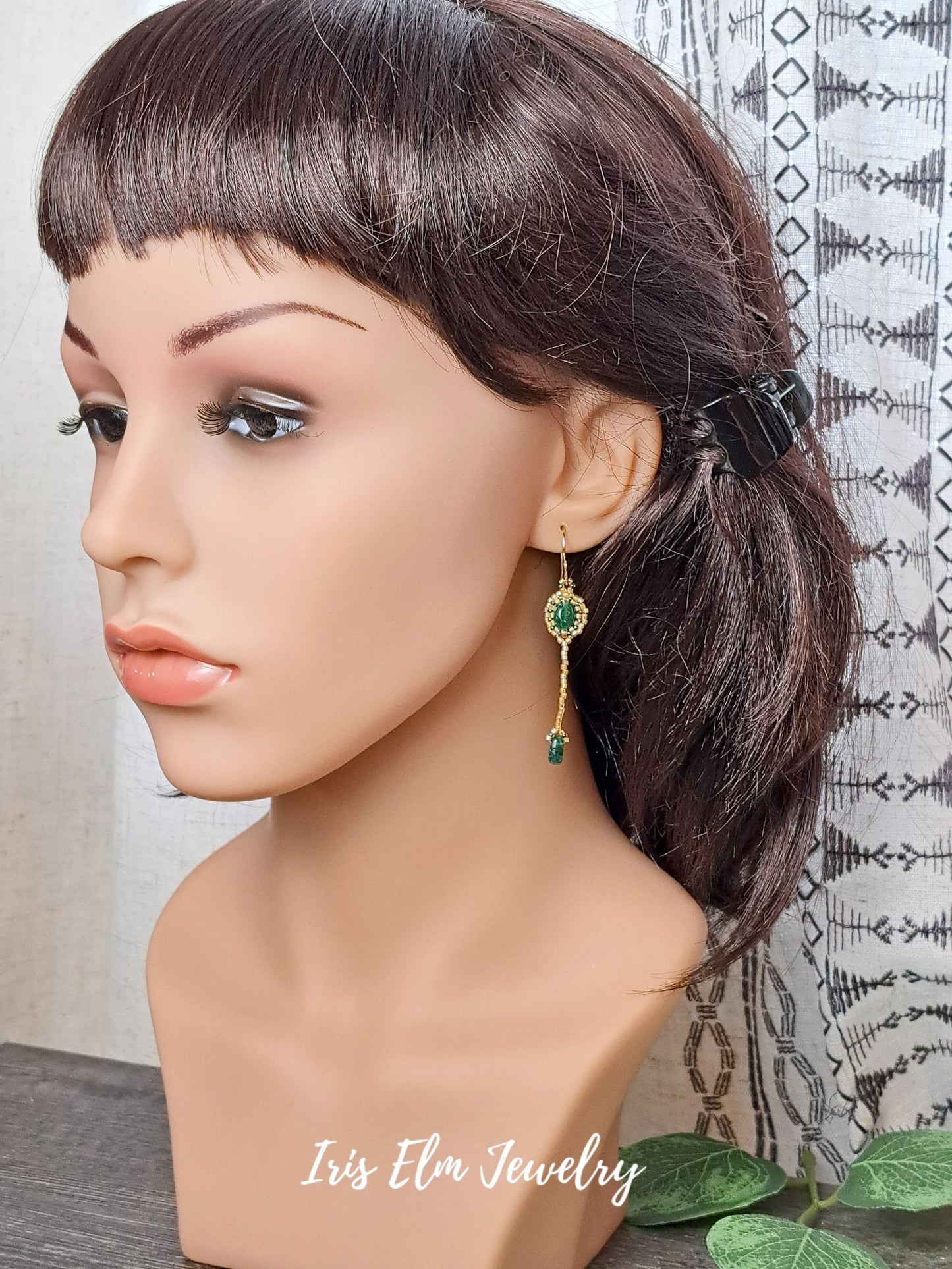 Mannequin head with dark hair styled in a ponytail, wearing a green aventurine earring, with 'Iris Elm Jewelry' branding.