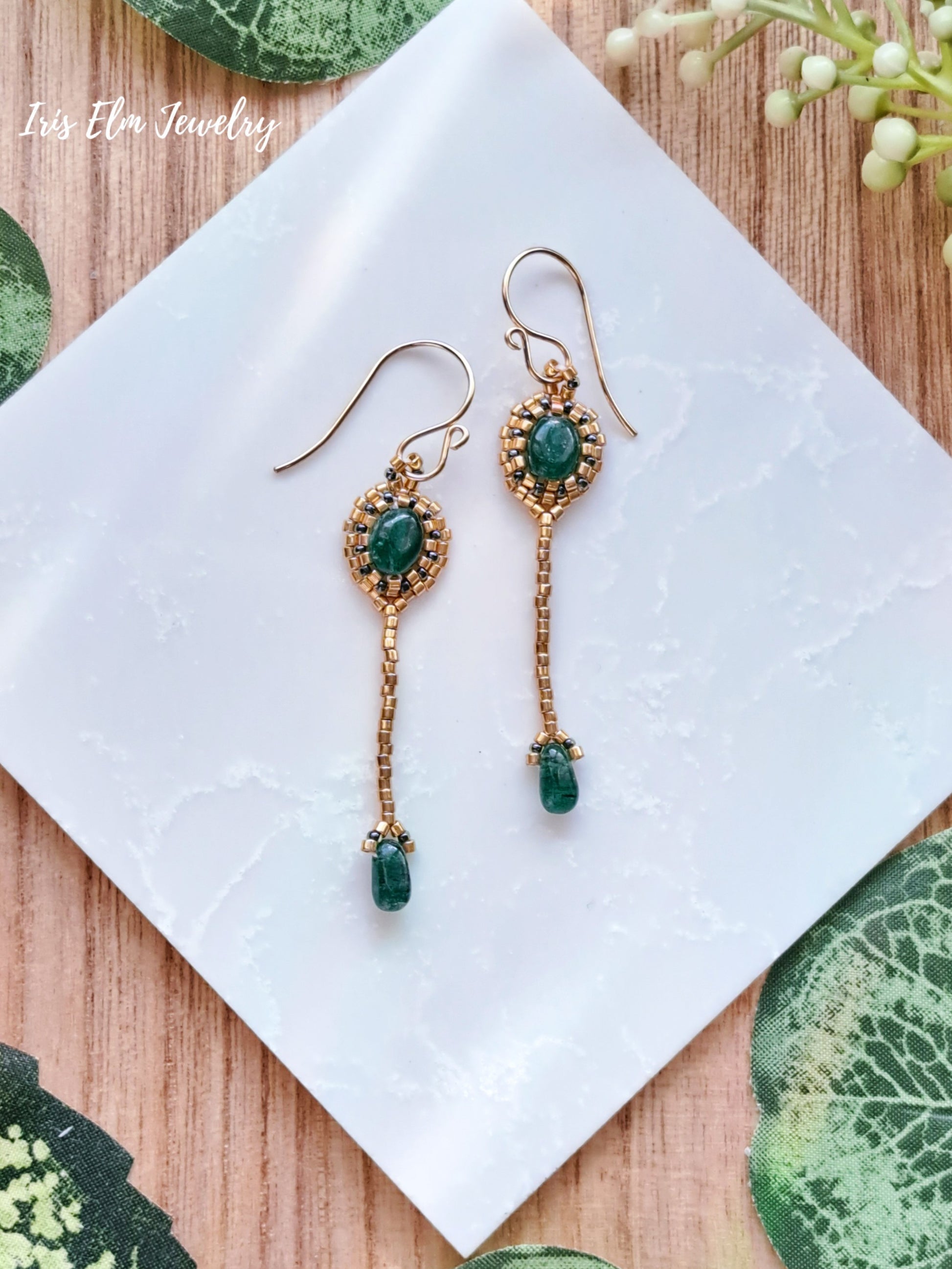 Gold art deco beadwork earrings with green aventurine gemstones on a white napkin with floral decorations.