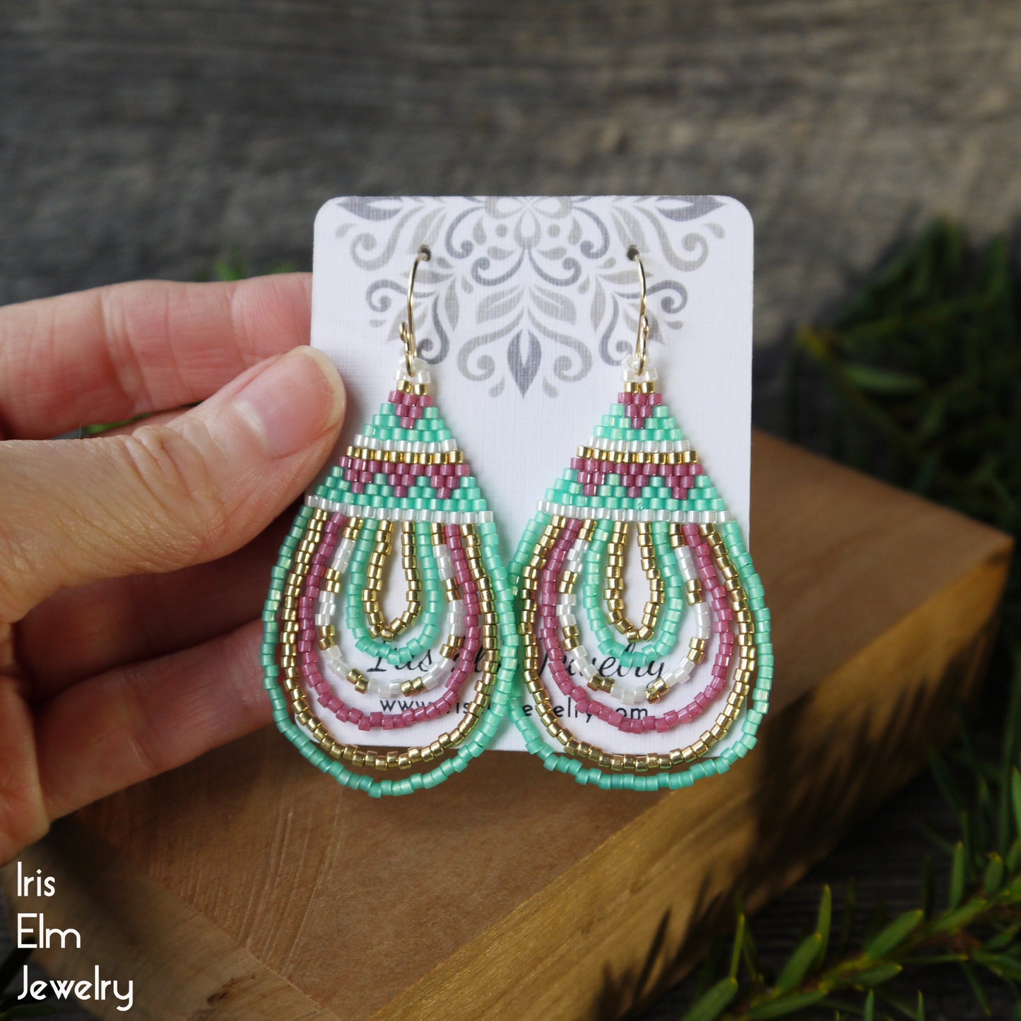 Colorful beaded seed bead teardrop earrings on a card held by a hand with a natural background