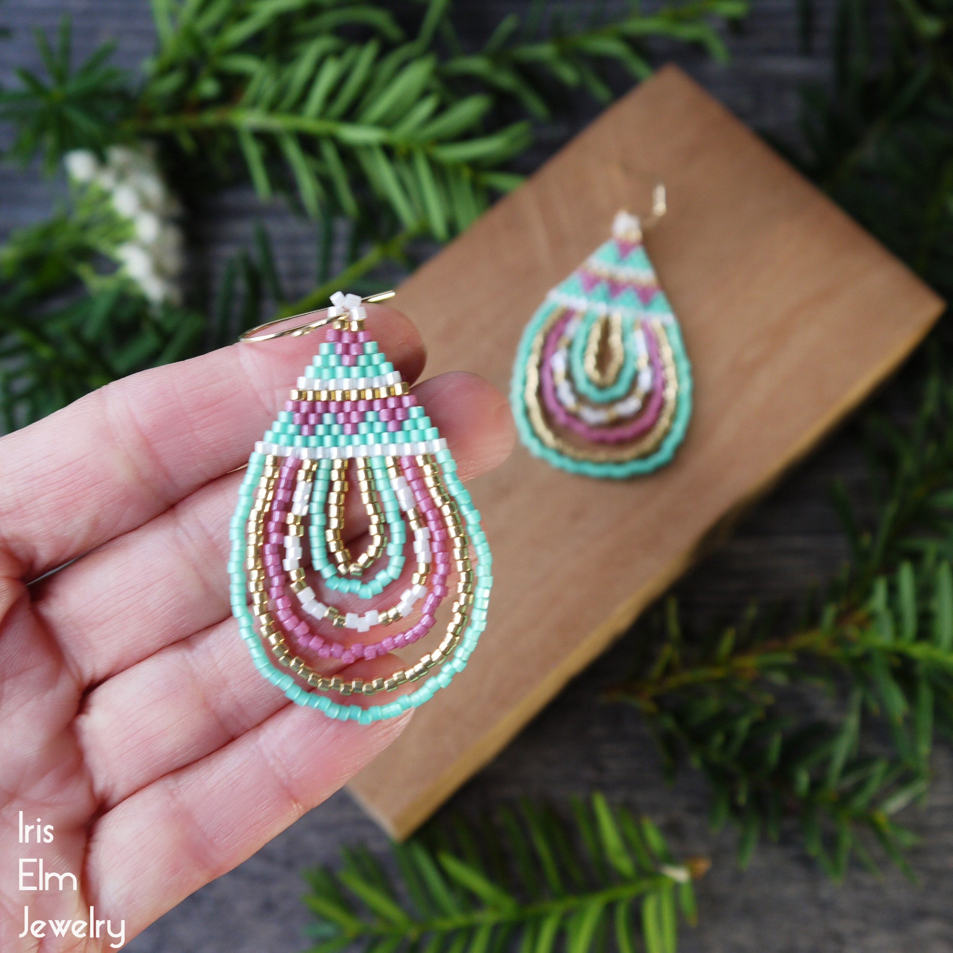 Colorful beadwoven seed bead pink and green glass earrings held in a hand with a natural background