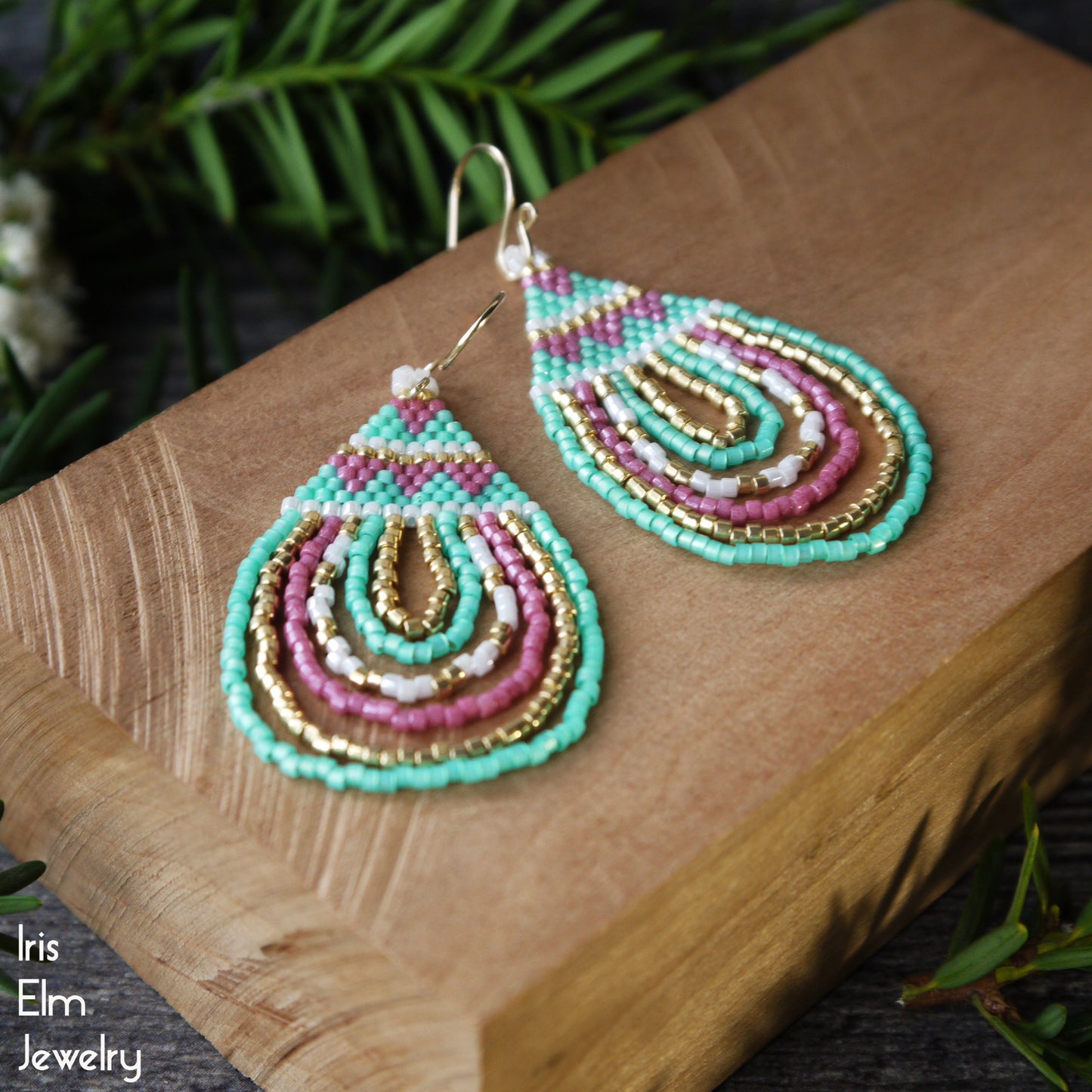 Colorful teardrop pink and mint green beaded handmade earrings on a wooden block with 'Iris Elm Jewelry' branding.