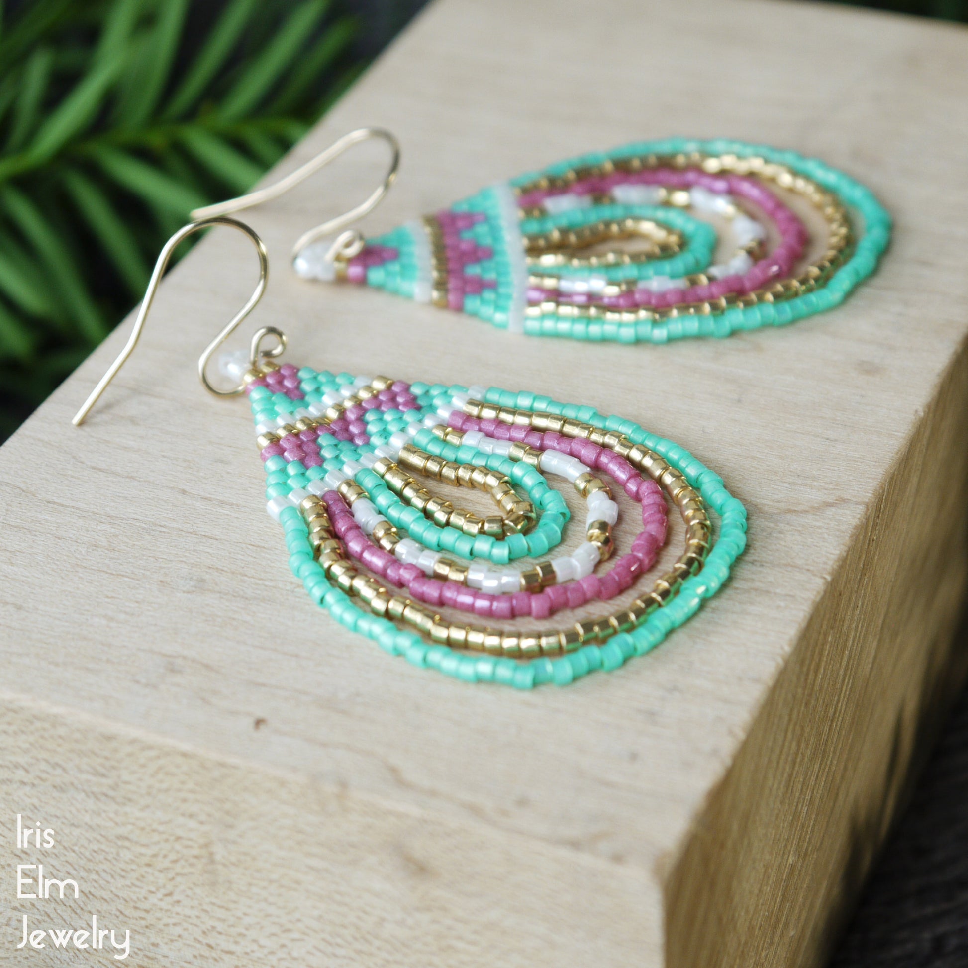 Beaded seed bead teardrop earrings on a wooden block with 'Iris Elm Jewelry' branding.