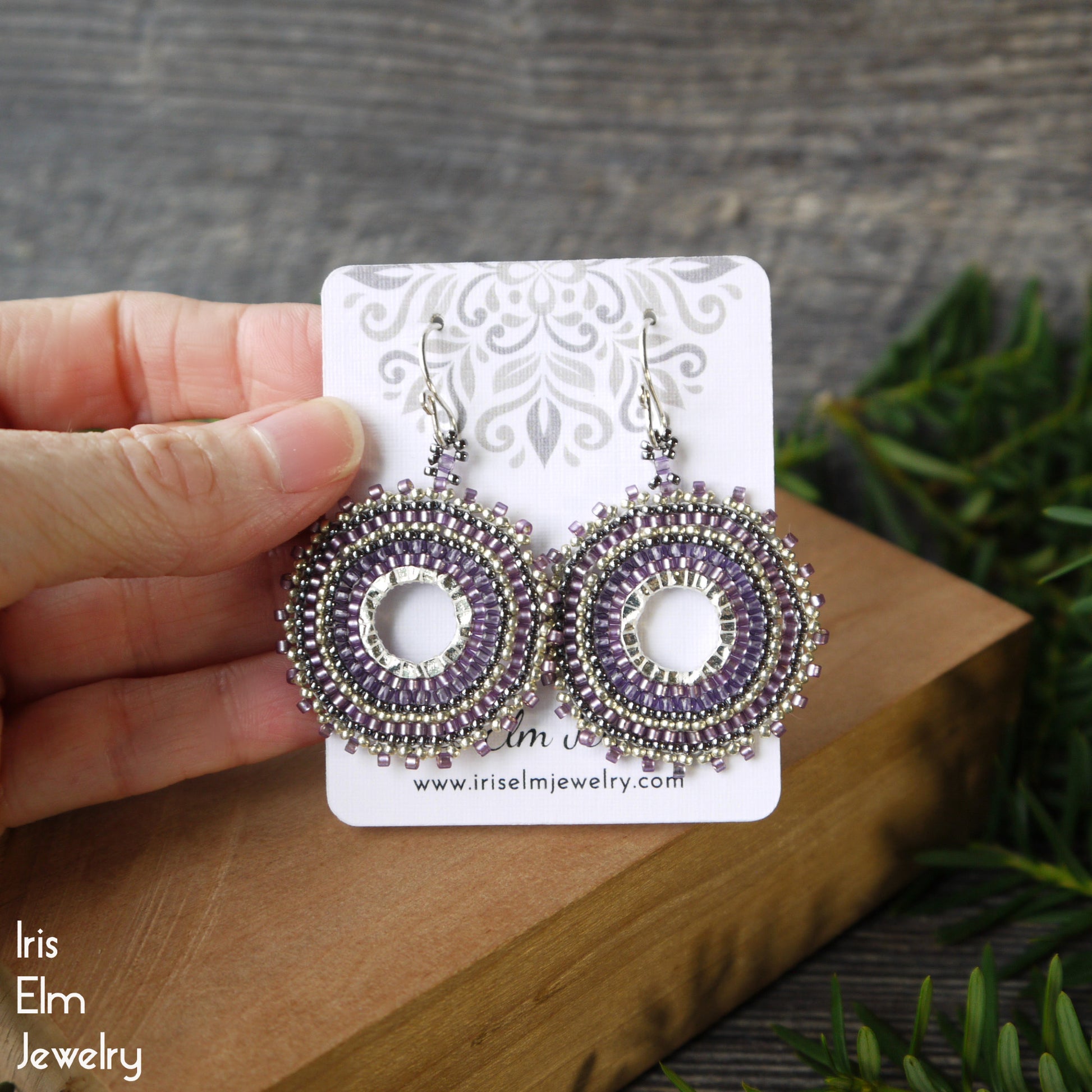 Purple and silver woven seed bead hoop earrings on a card held by a hand with a natural background