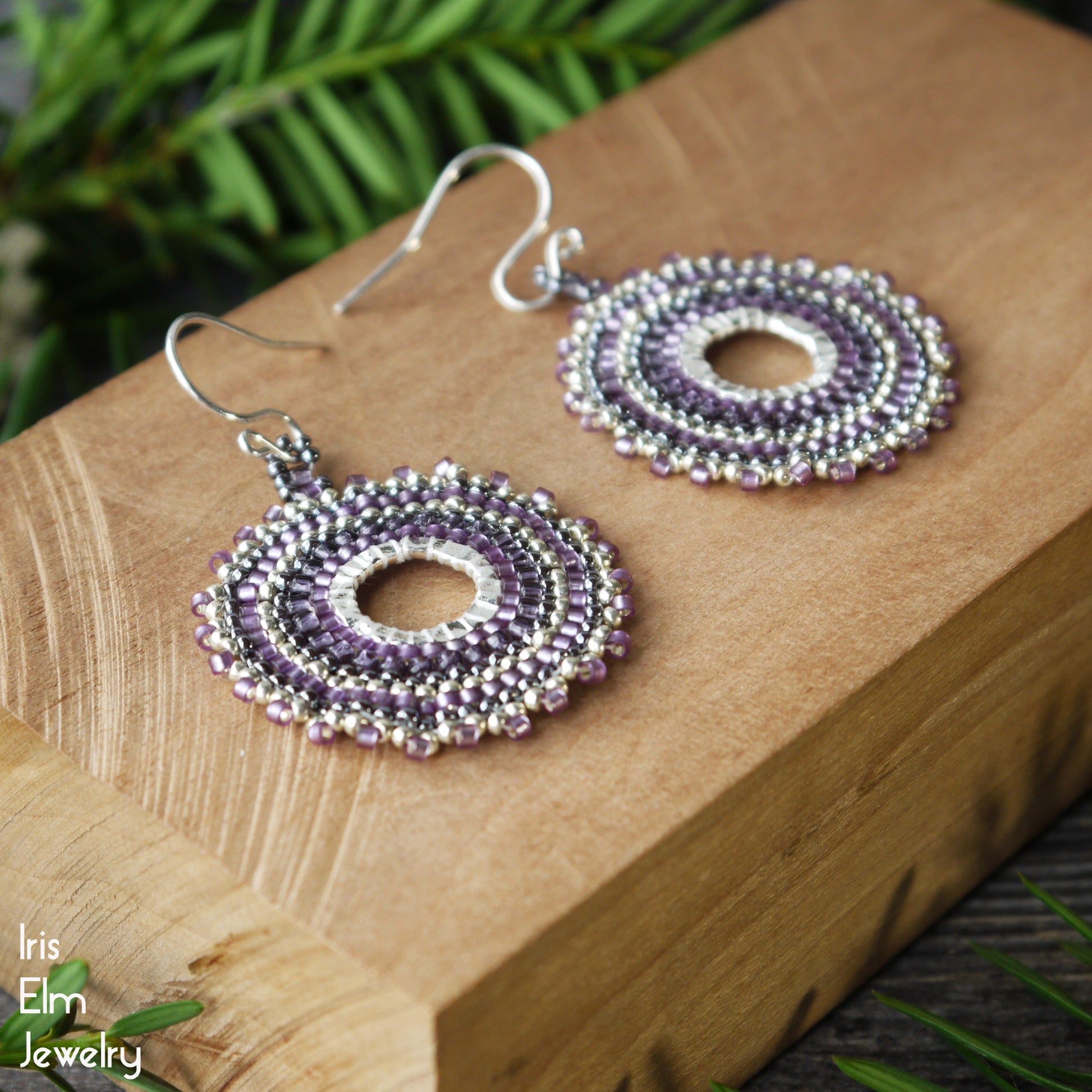 handmade Purple beaded hoop earrings with sterling silver ear wires on a wooden block with greenery in the background