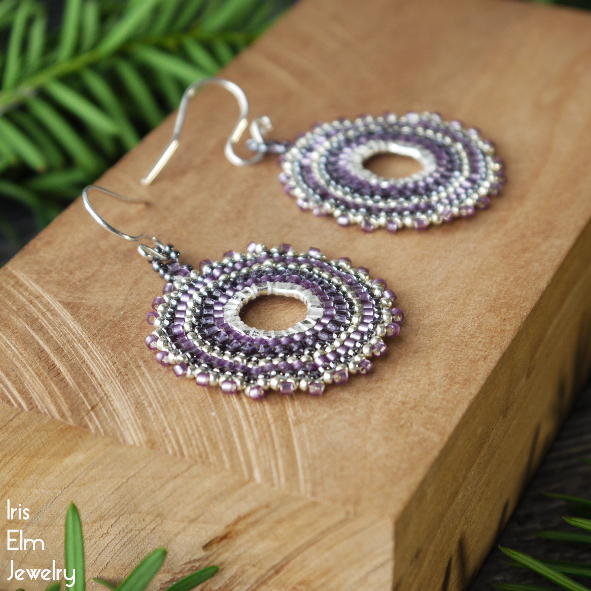 Purple beaded seed bead hoop earrings on a wooden surface with 'Iris Elm Jewelry' branding.