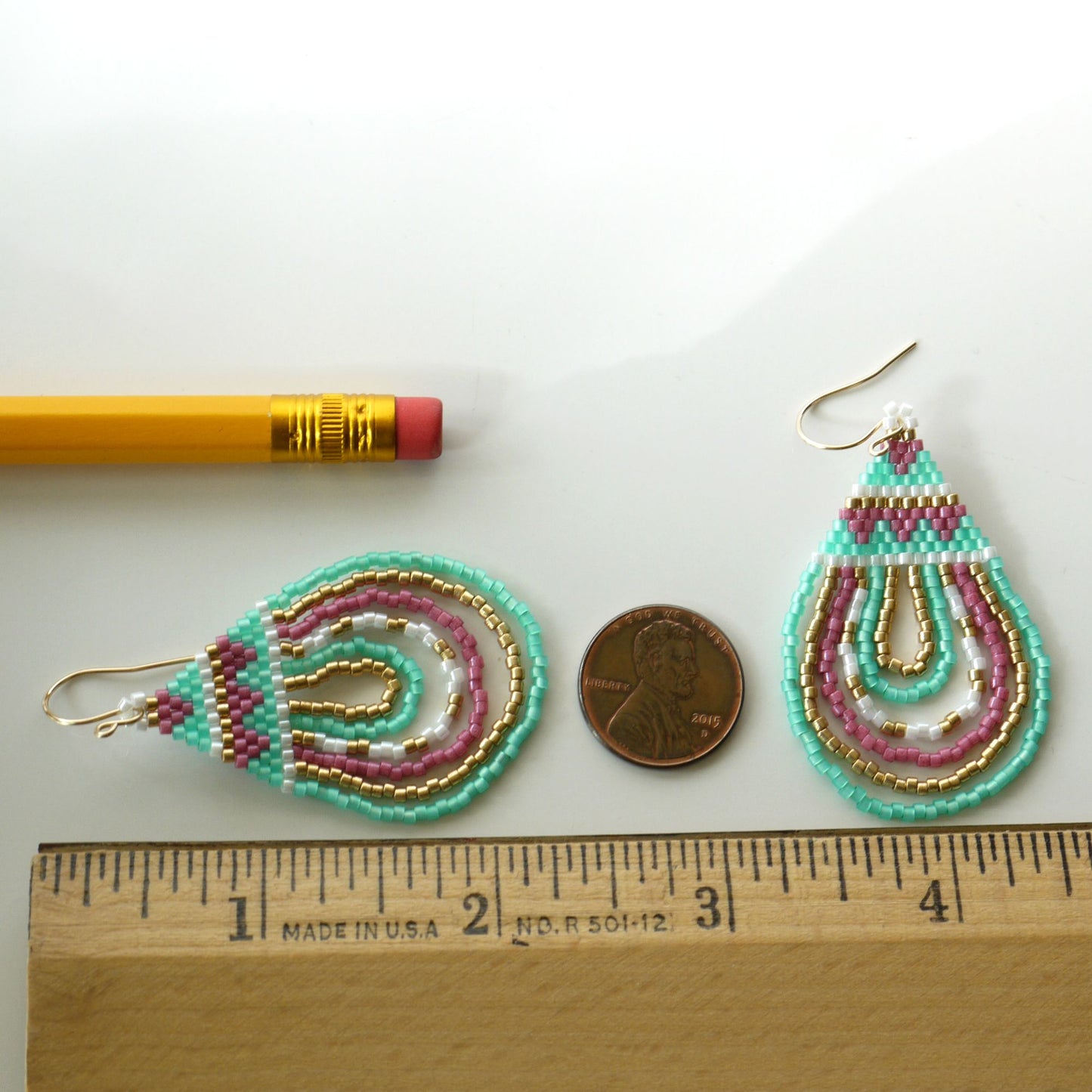 2.25 inch long Beaded teardrop seed bead earrings with a pencil and penny for scale on a white background