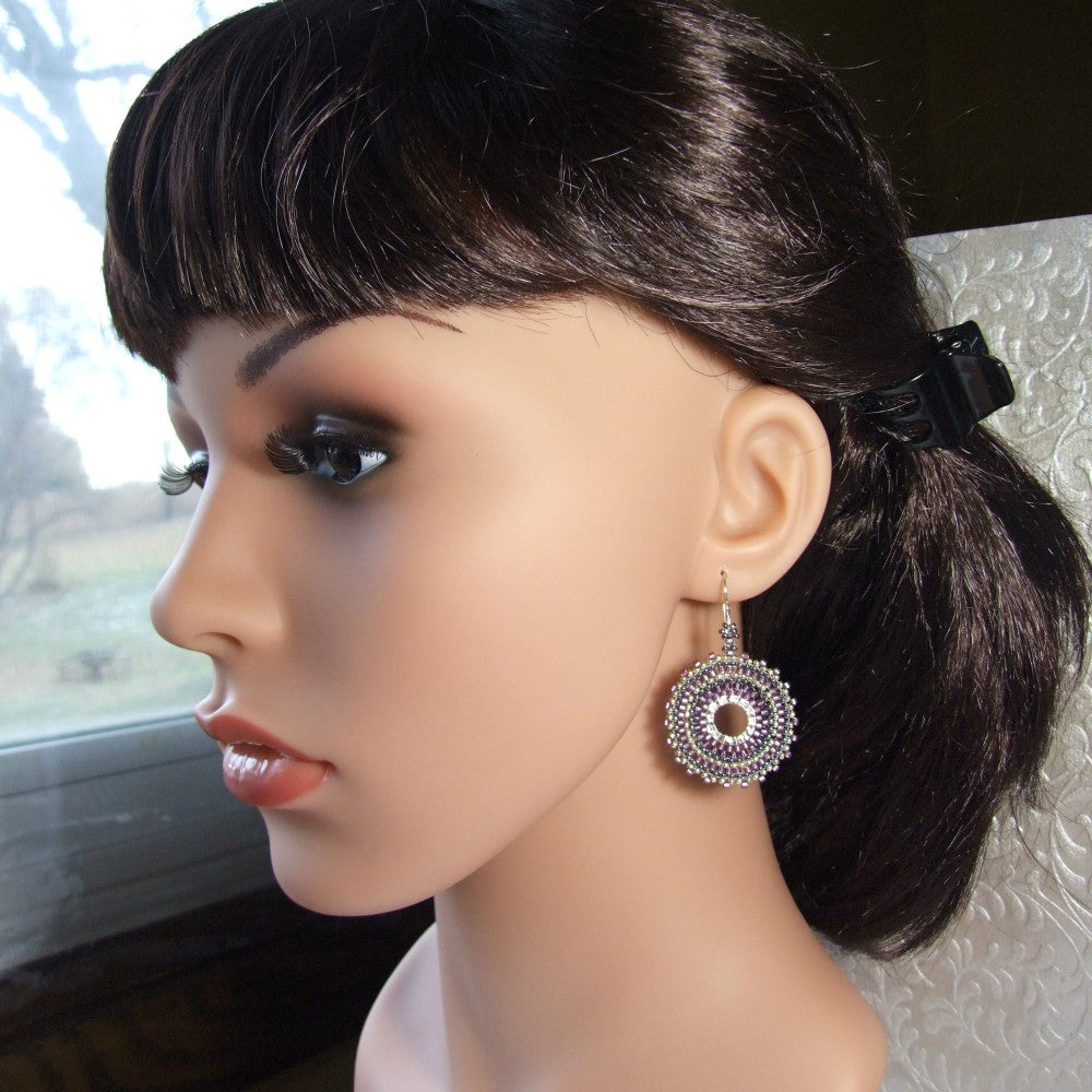 Mannequin head with dark hair styled in a ponytail and wearing purple and silver earrings.