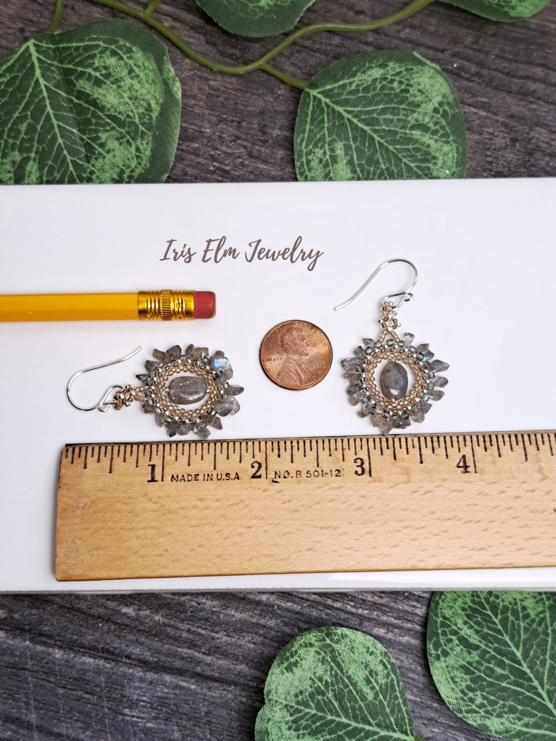 Pair of 1 and 7/8 inch long earrings on a card with a ruler for scale, surrounded by green leaves.