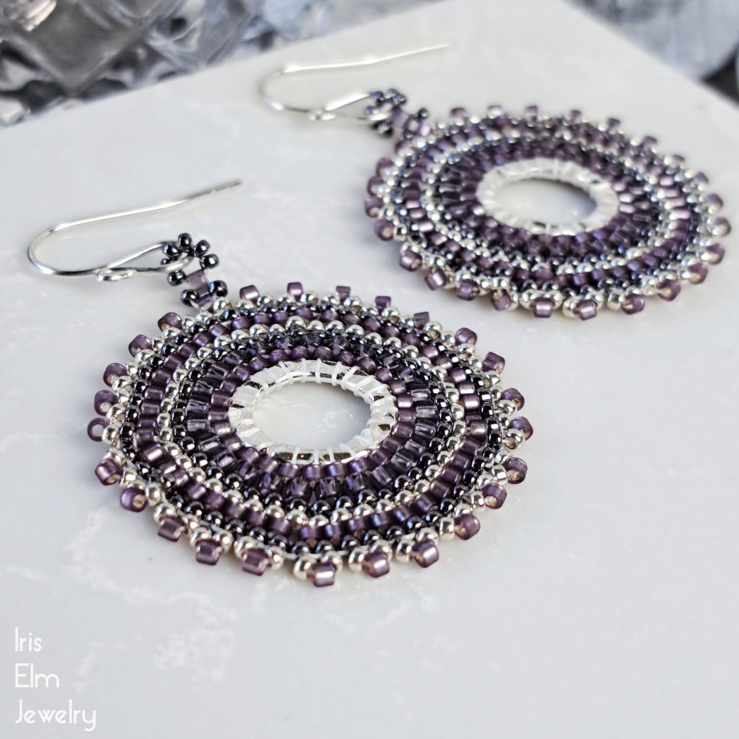 Purple glass seed bead beaded hoop earrings on a white surface with 'Iris Elm Jewelry' branding.