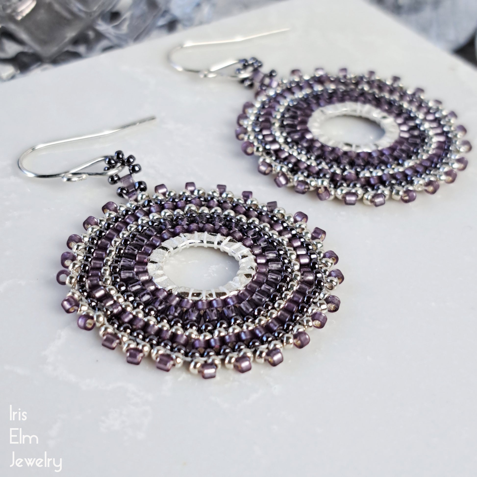 Purple glass seed bead beaded hoop earrings on a white surface with 'Iris Elm Jewelry' branding.