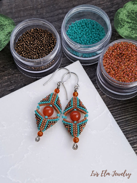 Beaded carnelian gemstone and seed bead beadwork earrings with colorful beads in small containers on a white surface.