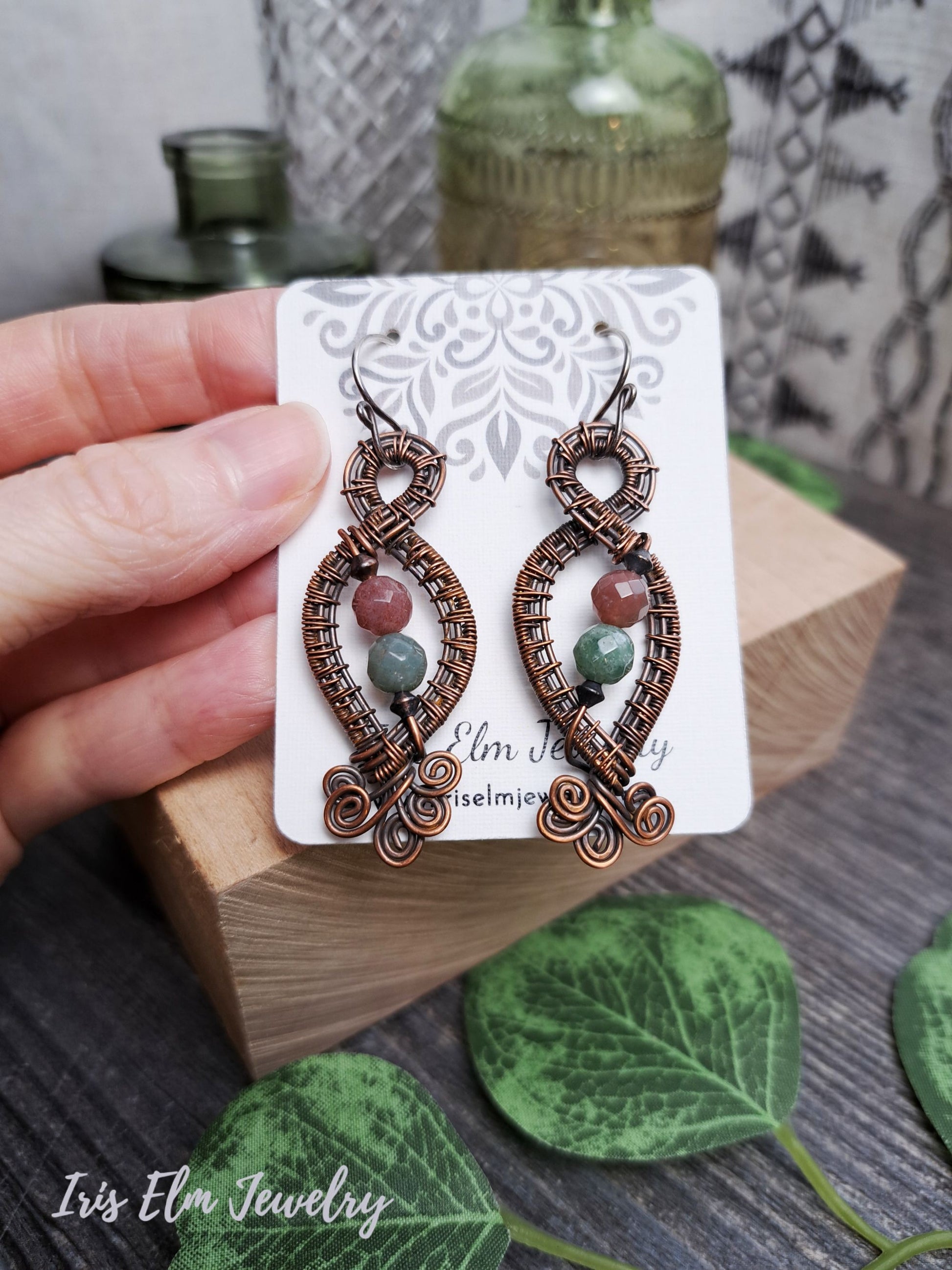 Decorative copper wire wrapped jasper handcrafted earrings on a card held by a hand with a natural background
