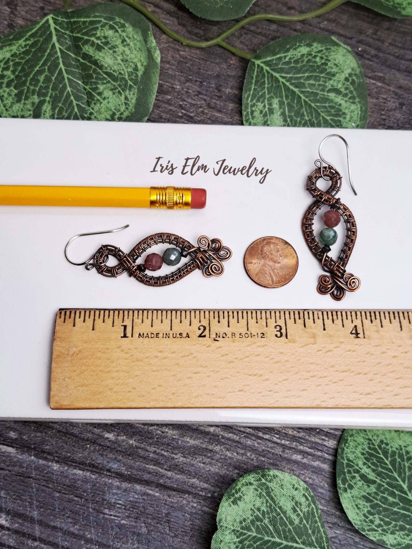 Pair of 2.25 inch long earrings on a white card with a ruler for scale, surrounded by green leaves.
