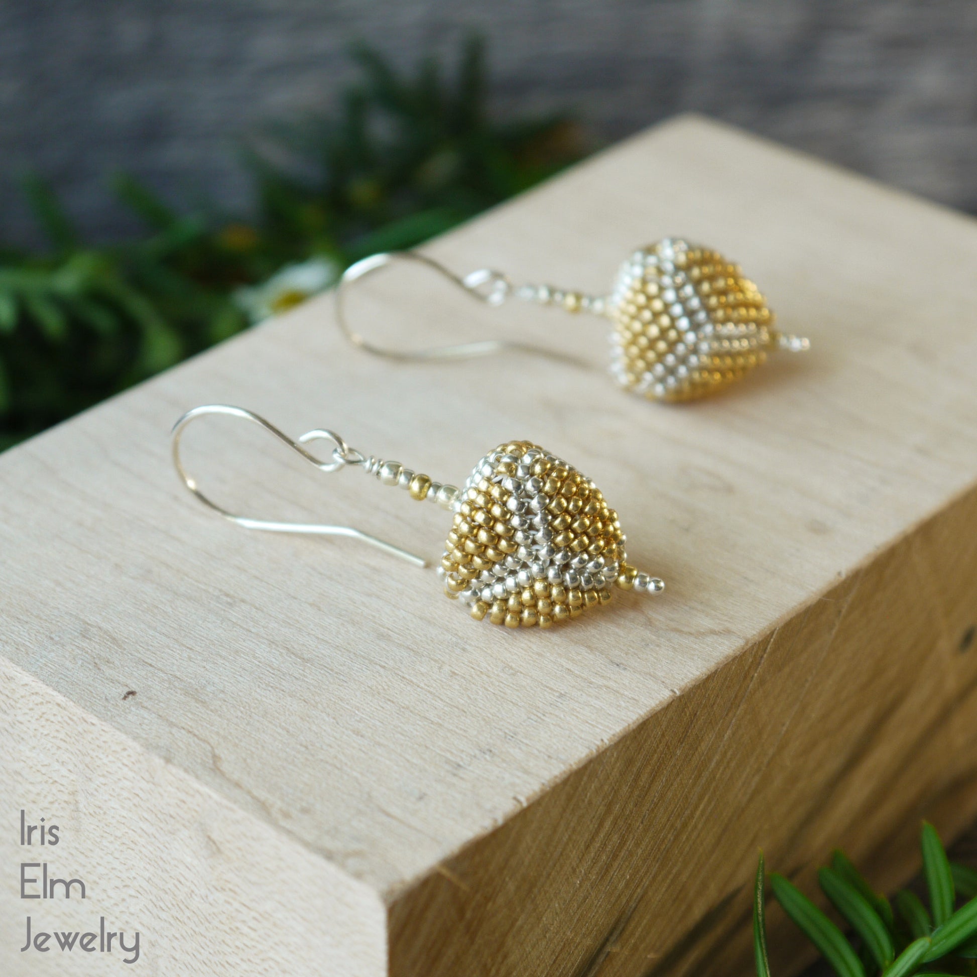 Gold and silver beaded triangle drop earrings on a wooden block with a blurred green background