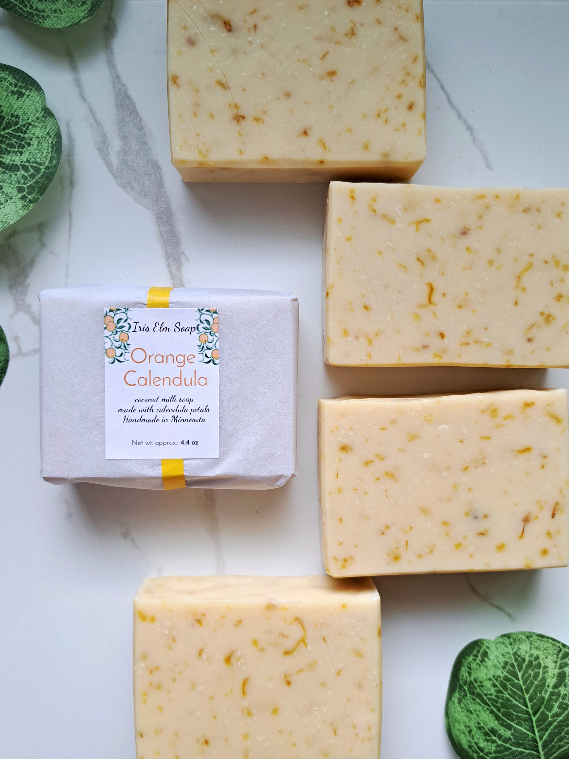 Orange Calendula soap bars with a bar of soap on a white marble background