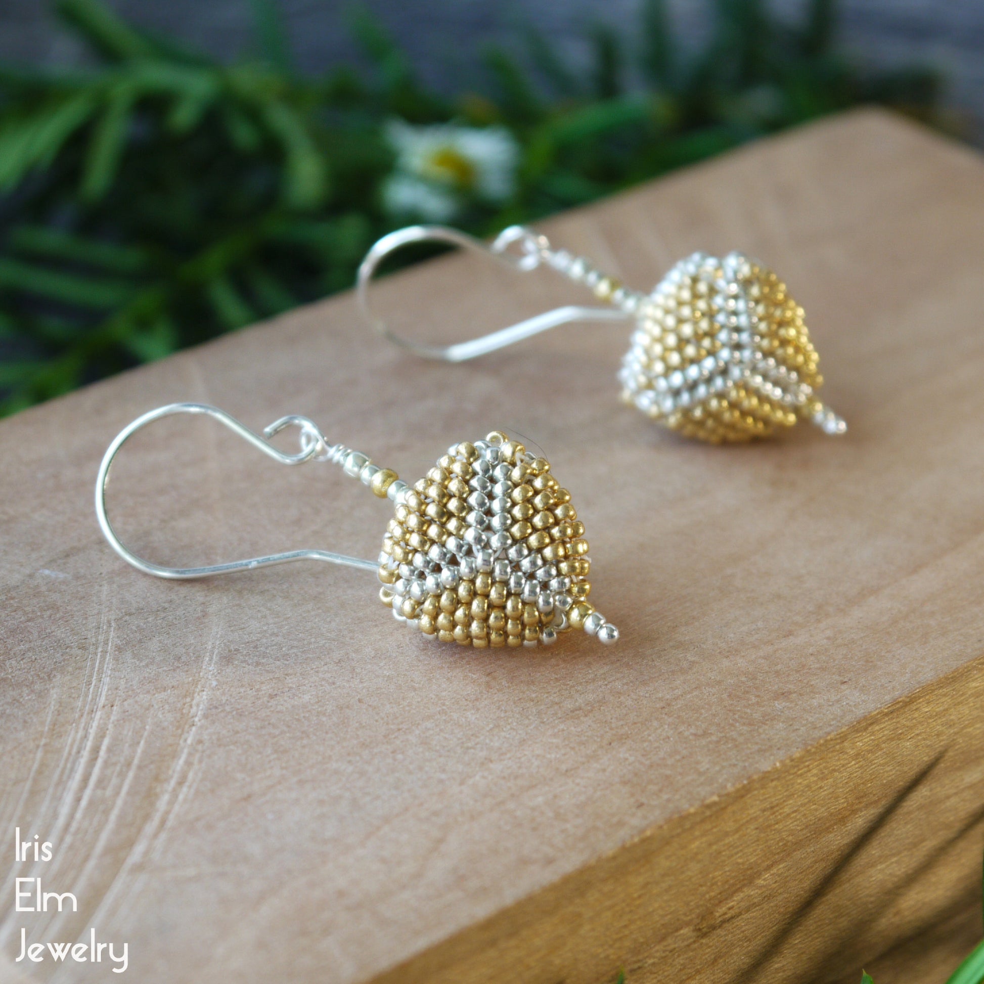 Pair of handmade gold and silver beaded earrings on a wooden surface with 'Iris Elm Jewelry' branding.