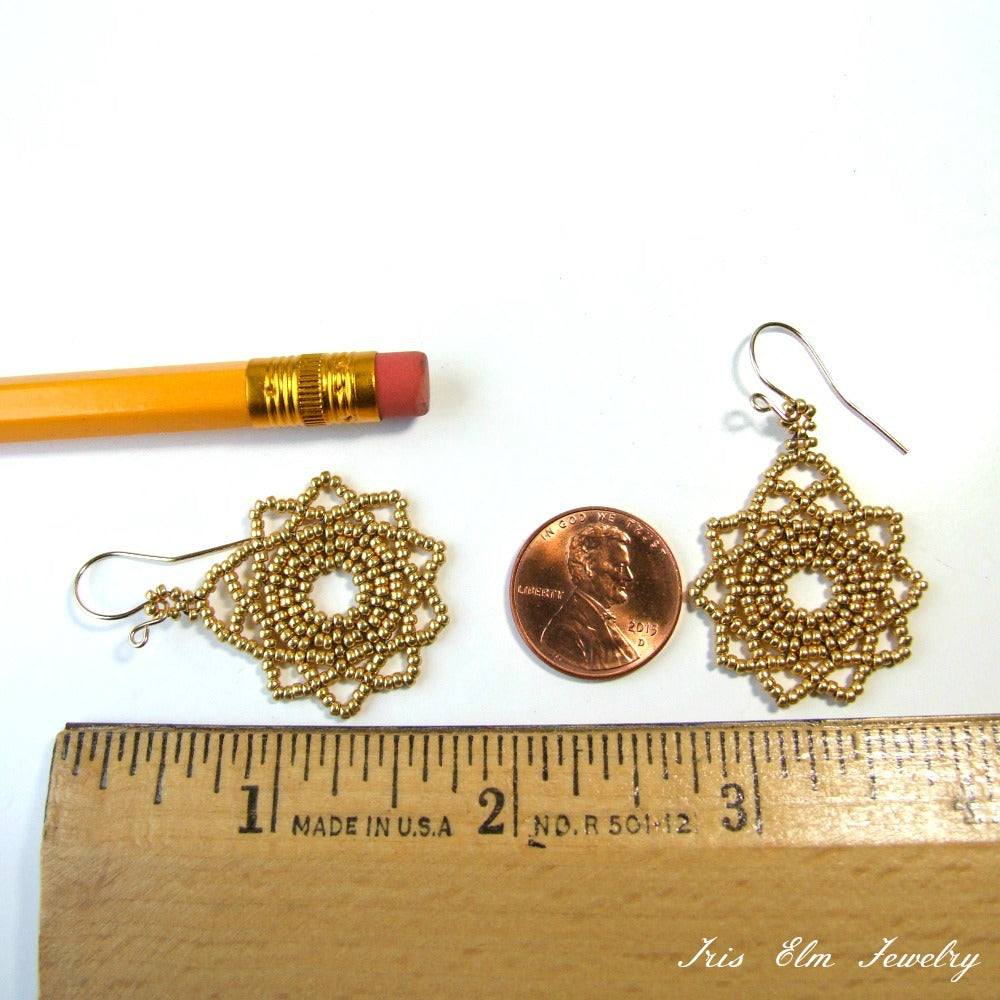 Gold seed bead mandala earrings next to a penny and a ruler for size comparison on a white background