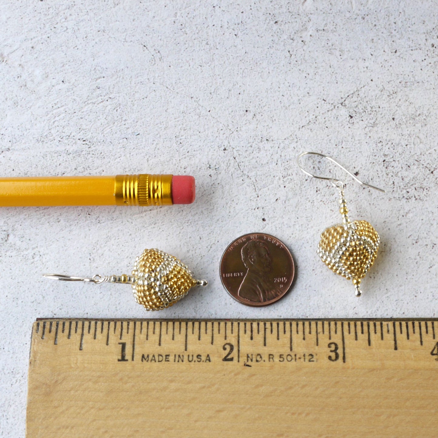 1.75 inch long Gold triangle shaped earrings next to a pencil, penny, and ruler for scale on a light gray background.