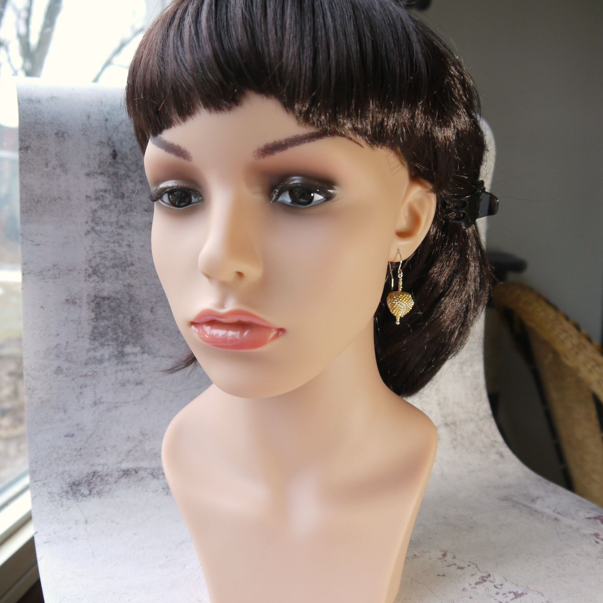 Mannequin head with a styled haircut and gold triangle seed bead earrings on a neutral background