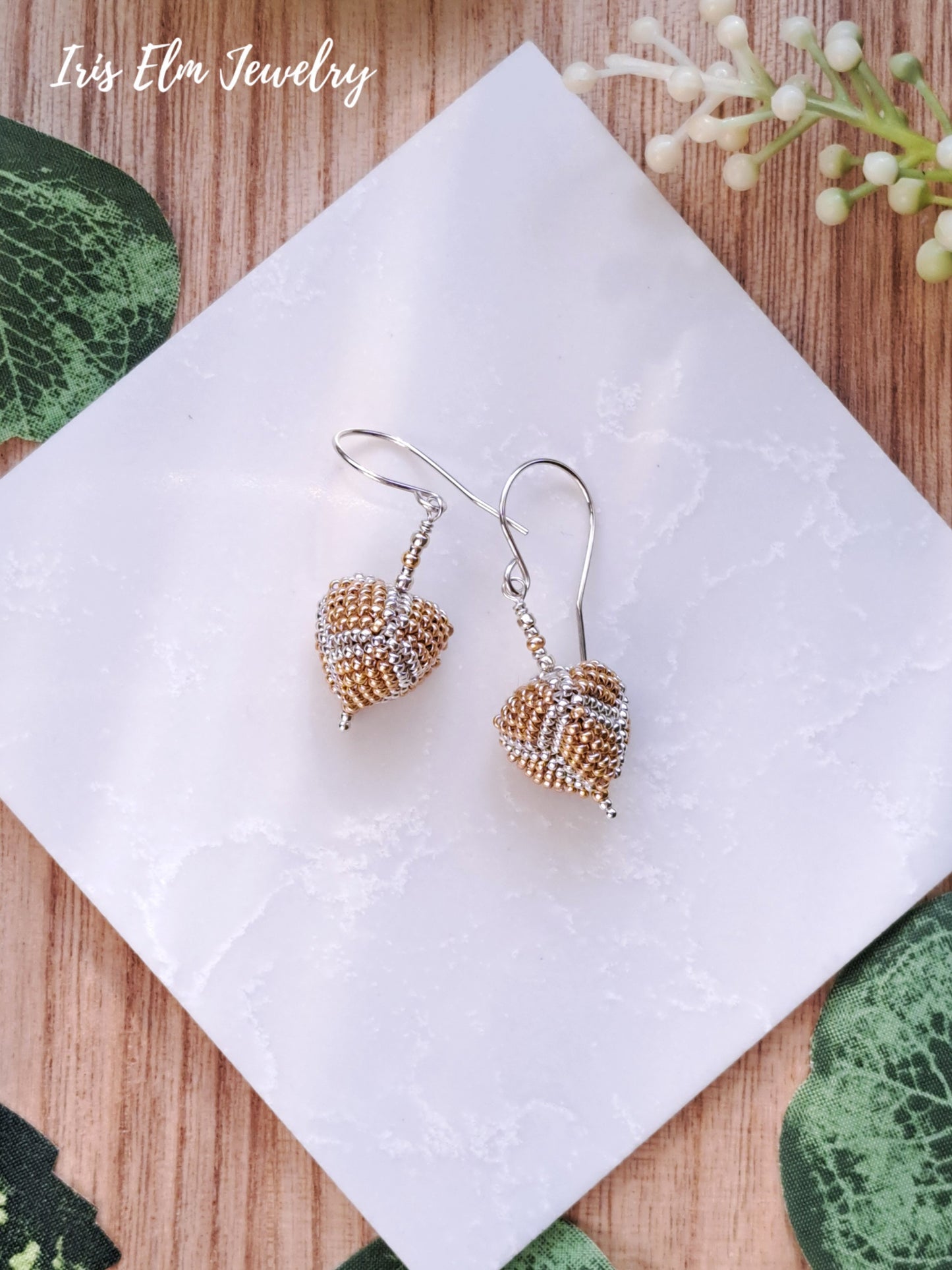 Pair of beaded gold and silver seed bead triangle-shaped earrings on a white napkin with 'Iris Elm Jewelry' branding.