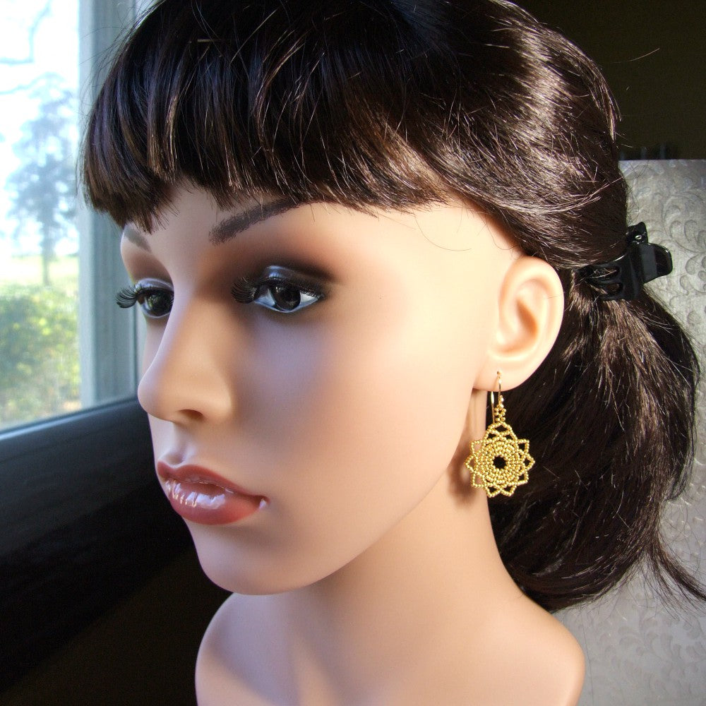 Mannequin head with dark hair and gold mandala earrings in a blurred indoor setting