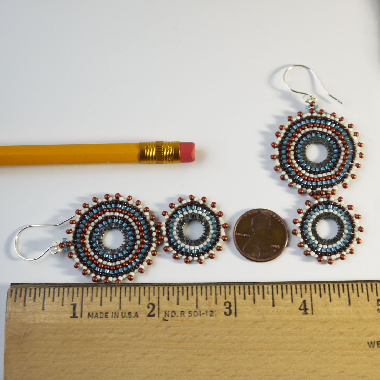 3 inch long handmade beaded hoop earrings with silver fishhook backs, displayed on a white background with a yellow pencil, a penny, and a wooden ruler for scale.