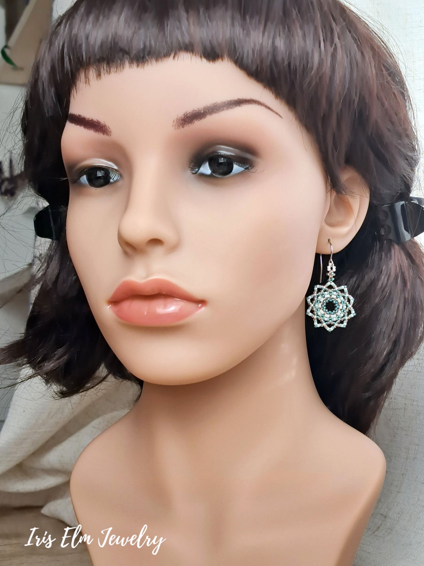 A close-up of a mannequin bust wearing a dangling silver-toned earring with a circular mandala design.