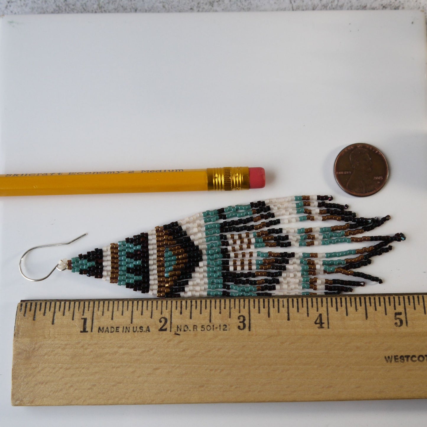 5 inch long Beaded fringe earring with geometric design next to a pencil, coin, and ruler for scale on a white background.