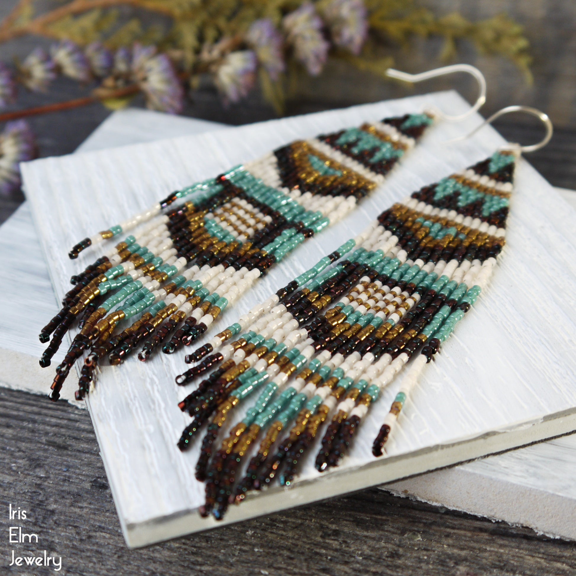 Pair of beaded fringe geometric seed  bead earrings on a white cloth with 'Iris Elm Jewelry' branding.