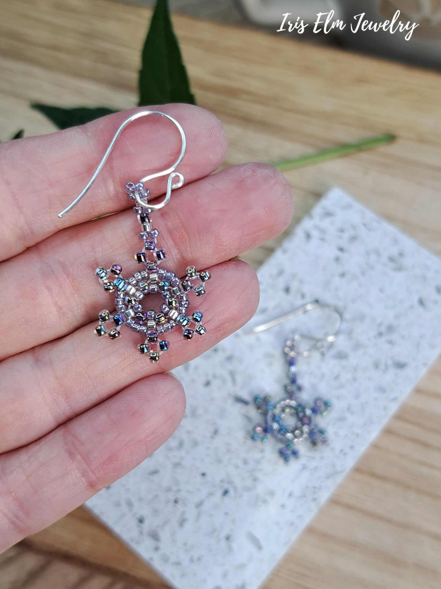 hand holding a iridescent purple seed bead snowflake earring