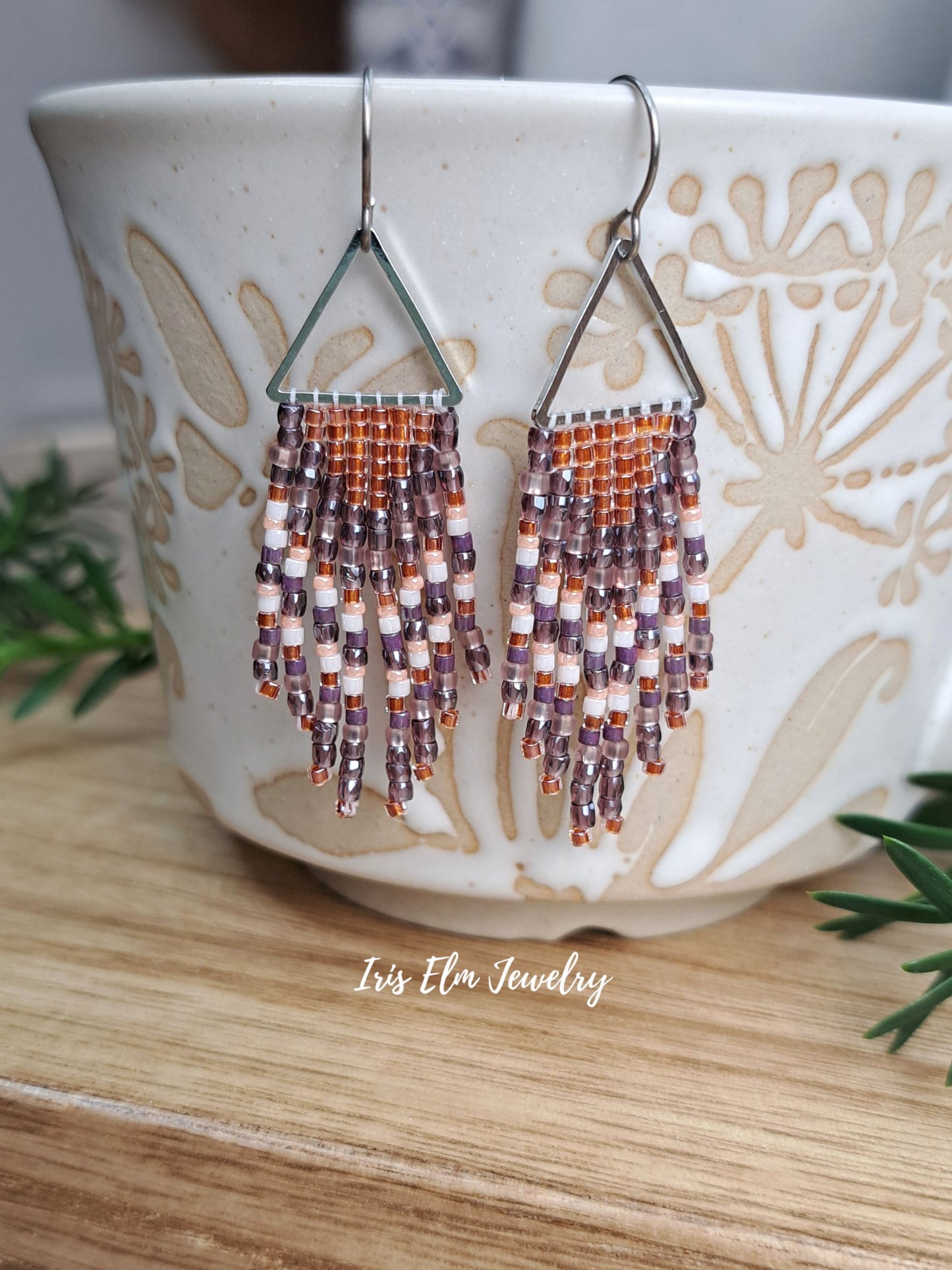 handmade small seed bead handwoven purple and copper orange seed bead fringe earrings dangling from ceremic cup with Iris Elm Jewelry branding.