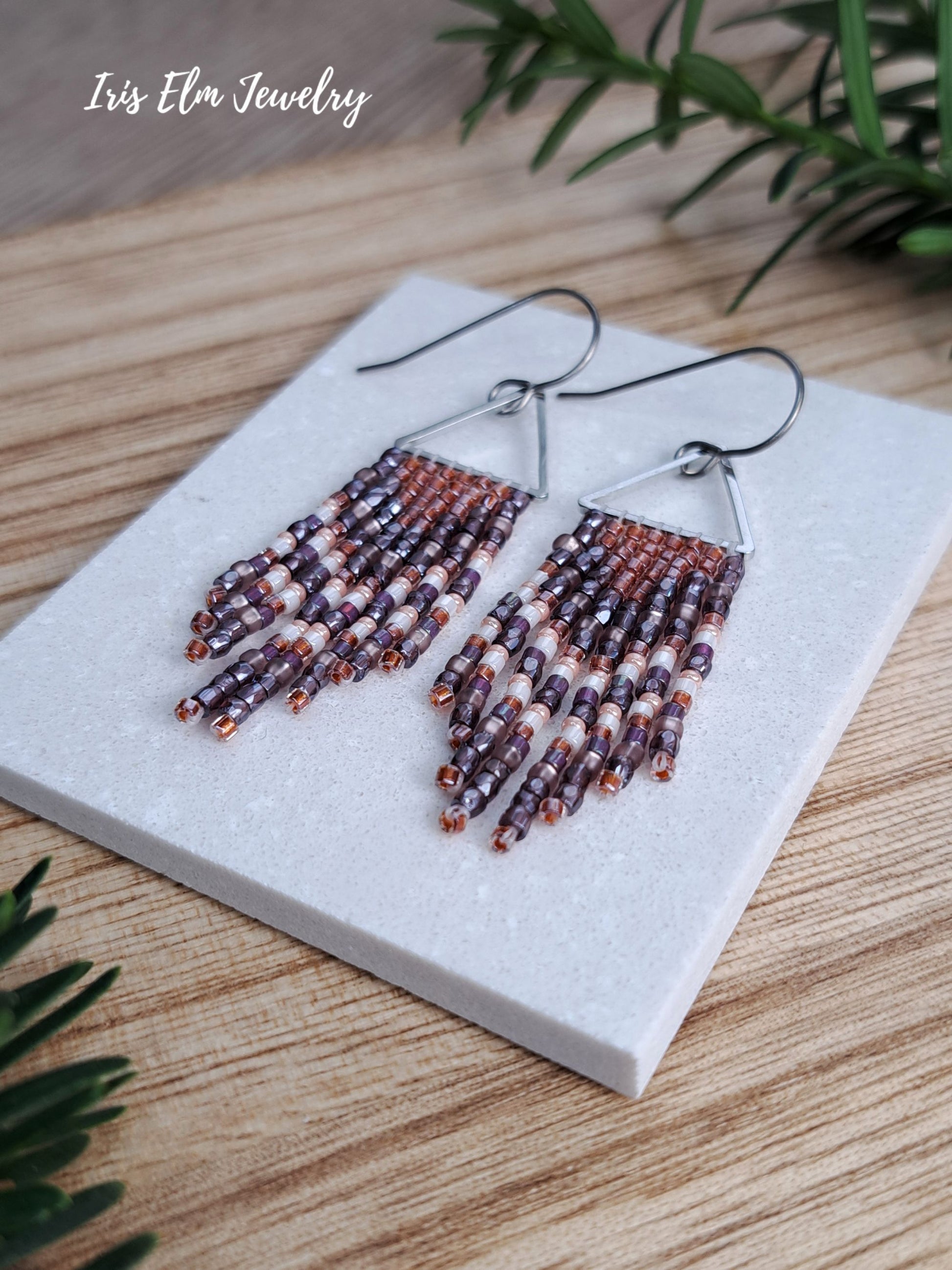 handmade small seed bead handwoven purple and copper orange seed bead fringe earrings on marble tile with Iris Elm Jewelry branding.