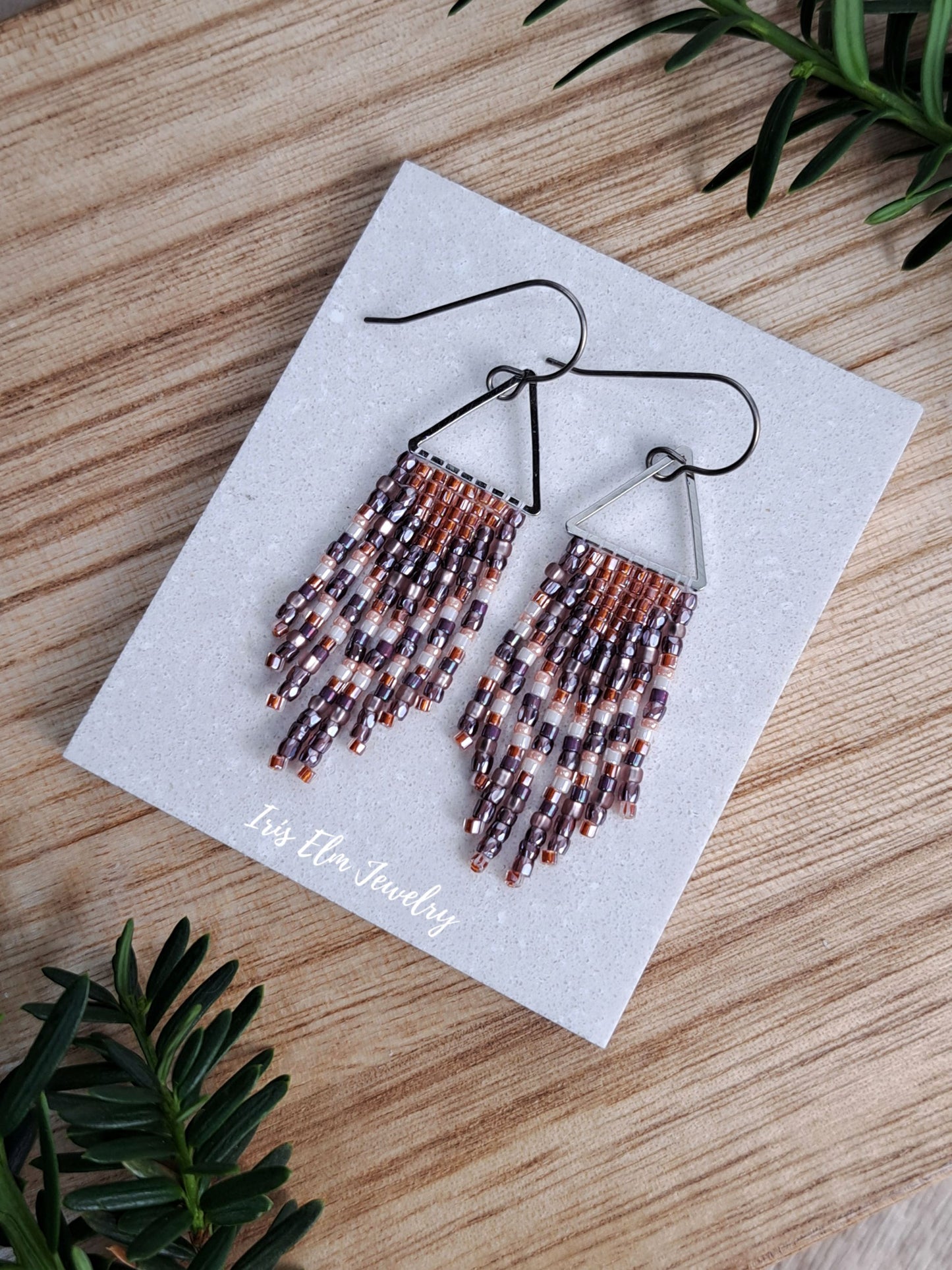 handmade small seed bead handwoven purple and copper orange seed bead fringe earrings on white tile surface with Iris Elm Jewelry branding.