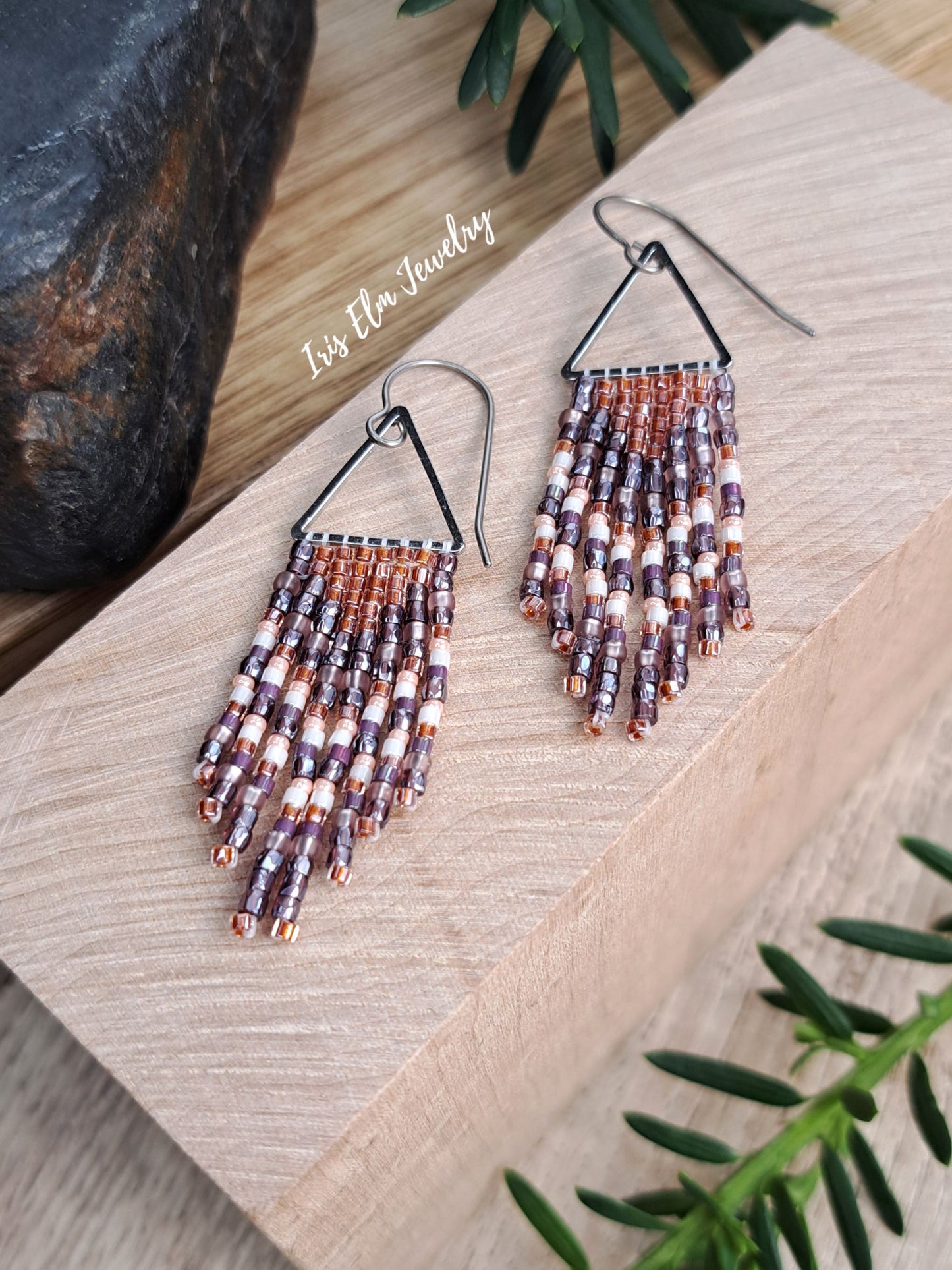 handmade small seed bead handwoven purple and copper orange seed bead fringe earrings on wooden surface with Iris Elm Jewelry branding.