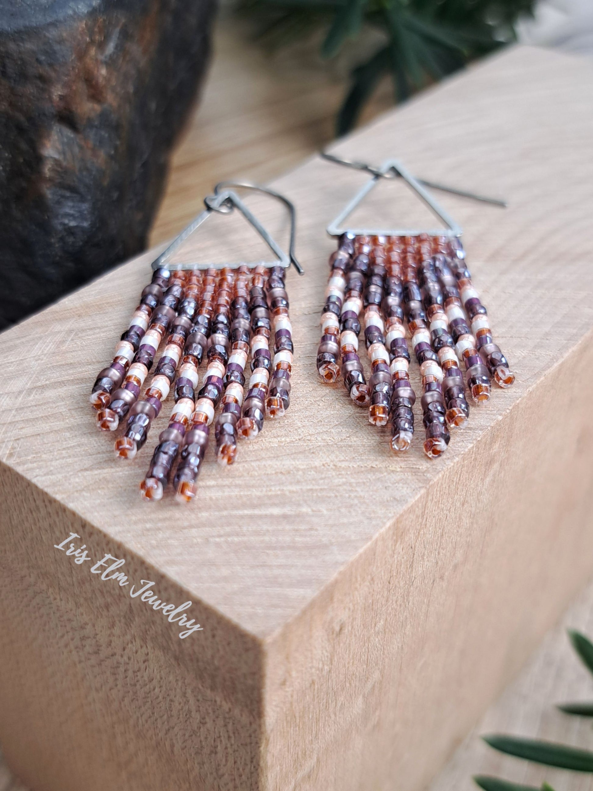 handmade small seed bead handwoven purple and copper orange seed bead fringe earrings on wooden surface with Iris Elm Jewelry branding.
