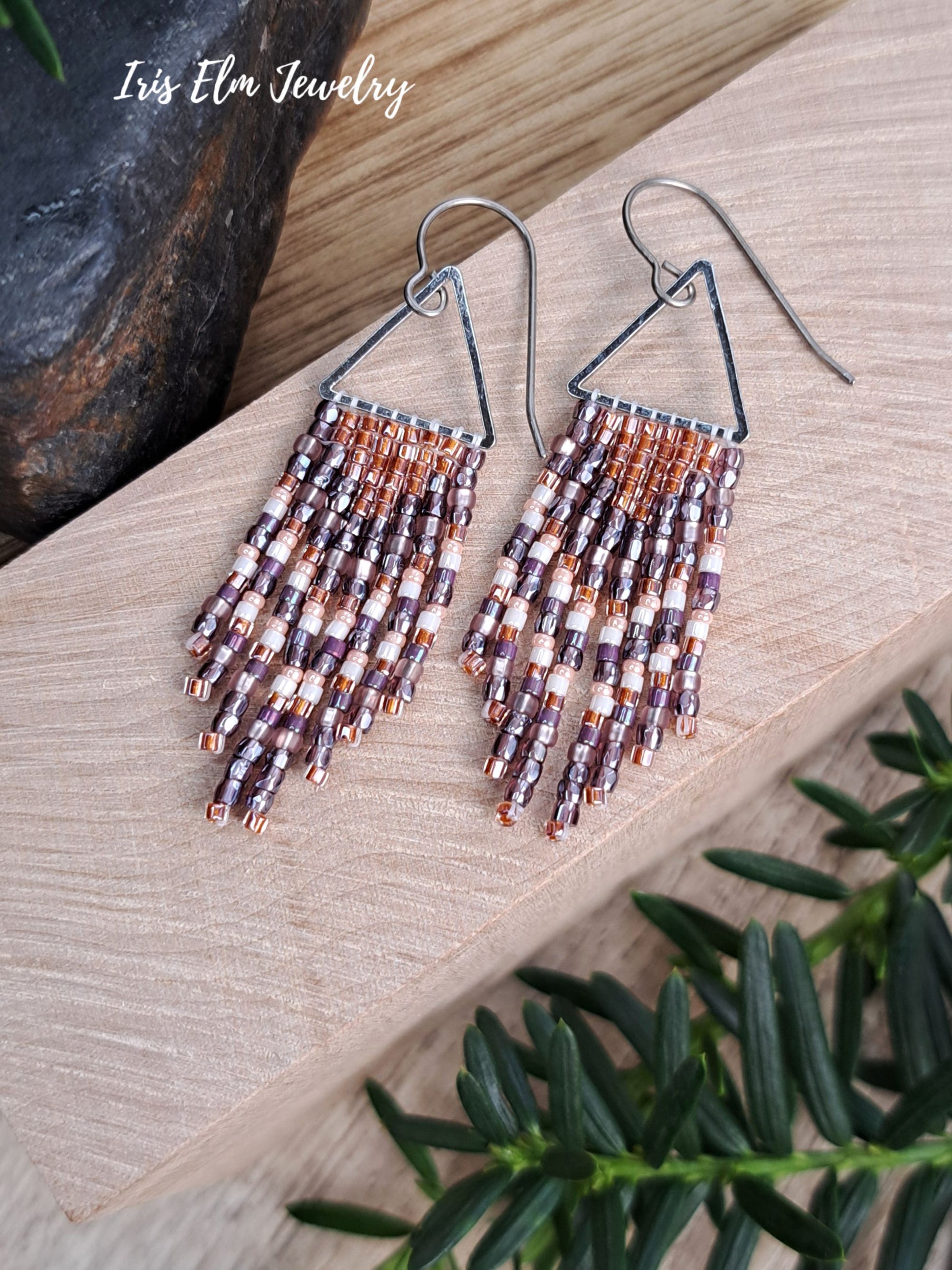 handmade small seed bead handwoven purple and copper orange seed bead fringe earrings on wooden surface with Iris Elm Jewelry branding.