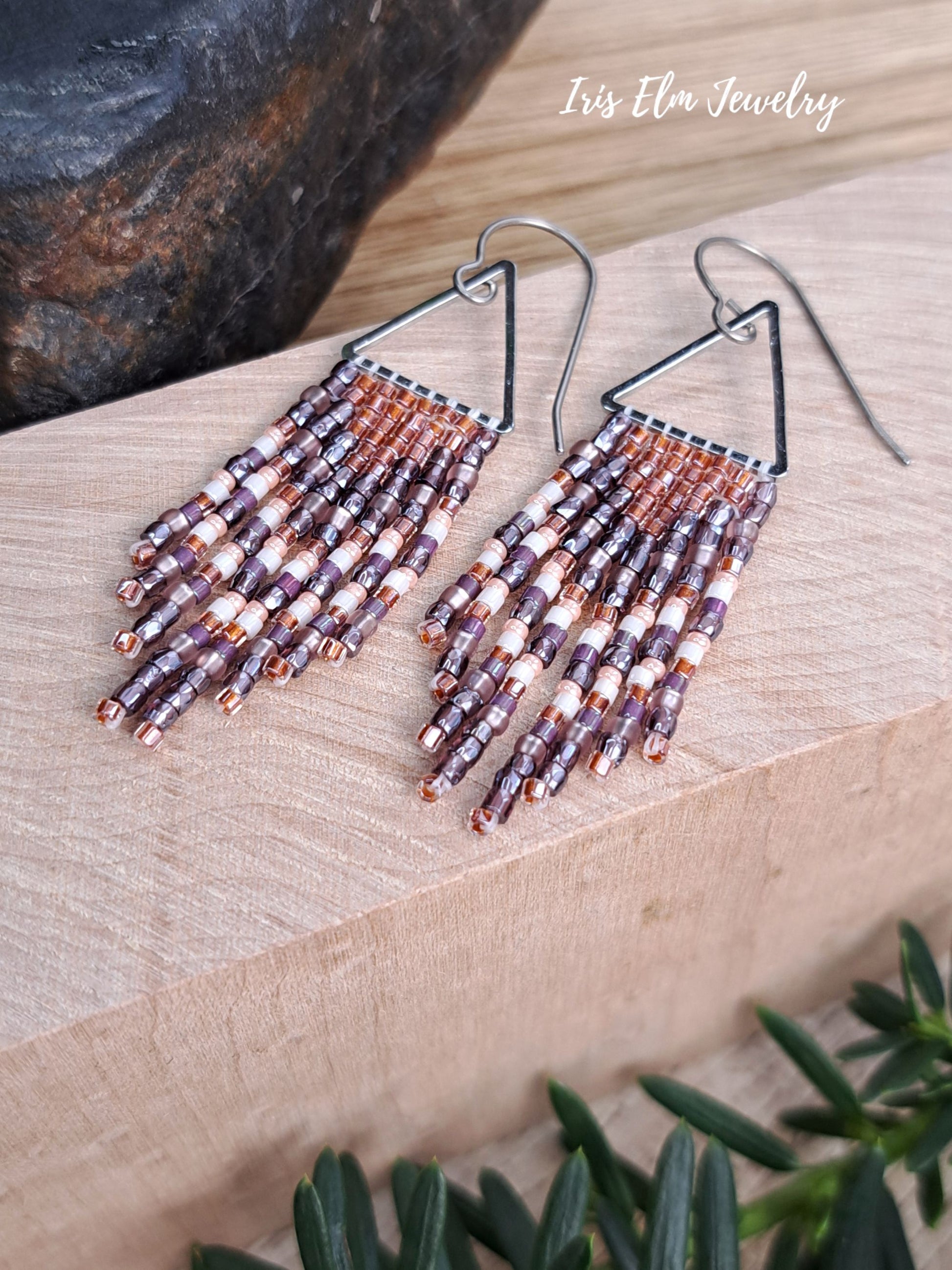handmade small seed bead handwoven purple and copper orange seed bead fringe earrings on wooden surface with Iris Elm Jewelry branding.