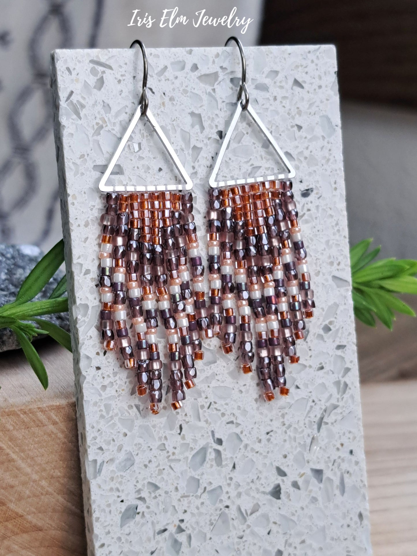 handmade small seed bead handwoven purple and copper orange seed bead fringe earrings on terrazzo tile surface with Iris Elm Jewelry branding.
