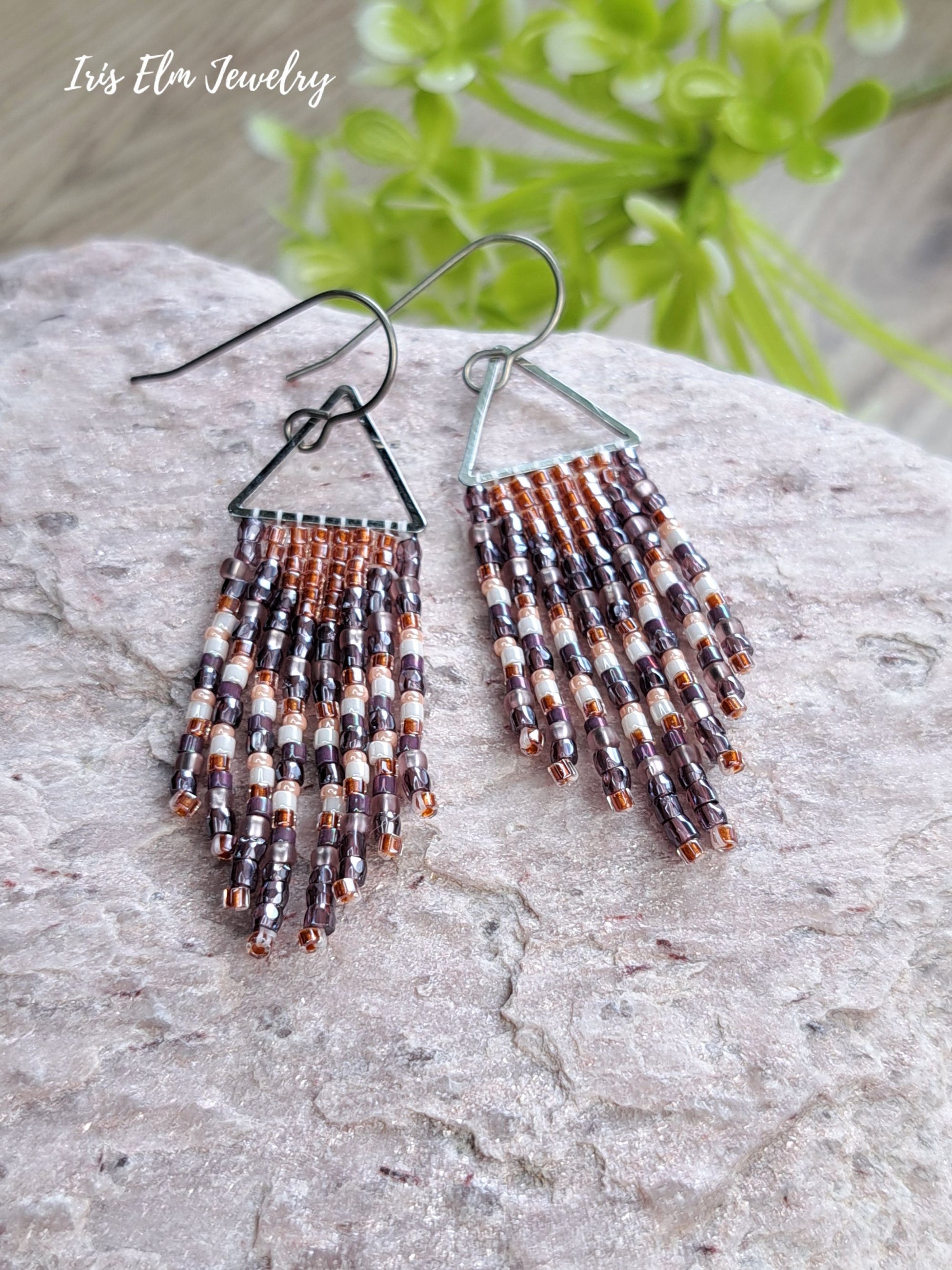 handmade small seed bead handwoven purple and copper orange seed bead fringe earrings on a rock with Iris Elm Jewelry branding.