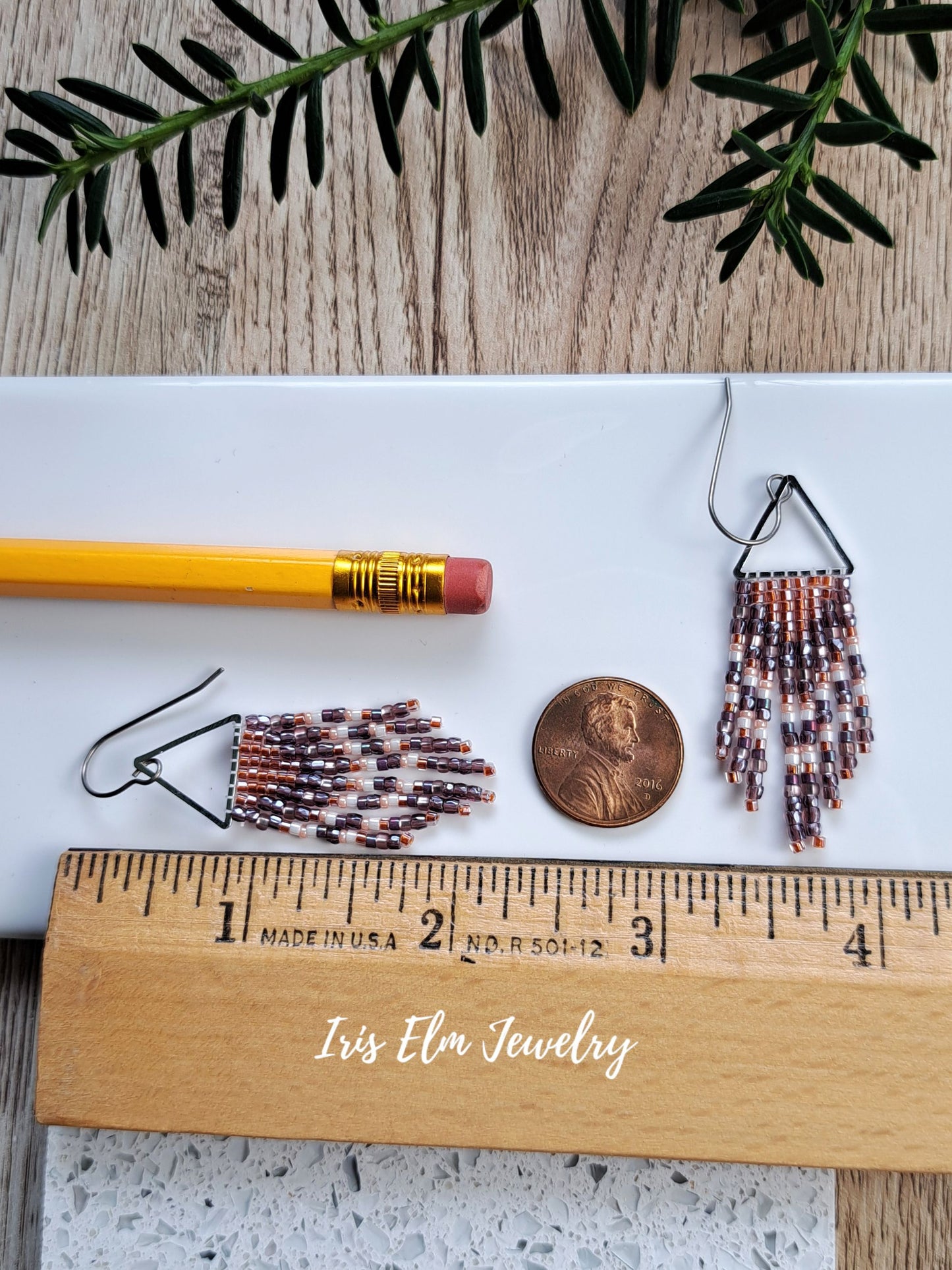 2.25 inch long handmade small seed bead handwoven purple and copper orange seed bead fringe earrings next to ruler, penny, and pencil for scale with Iris Elm Jewelry branding.