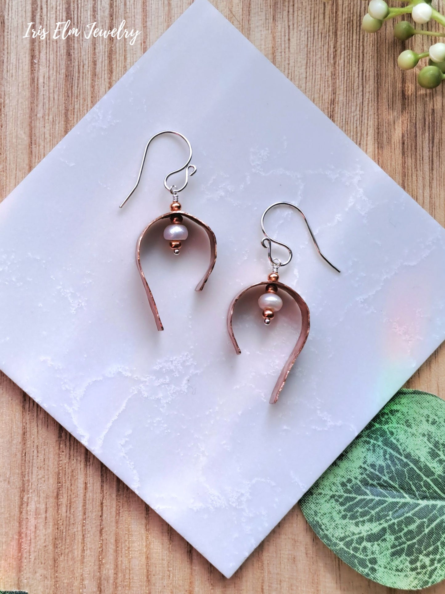 Pair of copper freshwater pearl earrings on a white tile with a wooden background